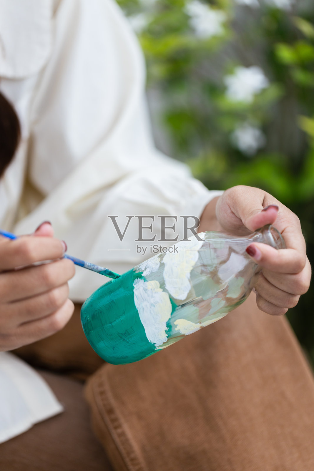 一个人通过用白色和绿色涂料绘制玻璃瓶，创造可持续和环保的手工艺术，表达对环境的创造力和关爱。照片摄影图片