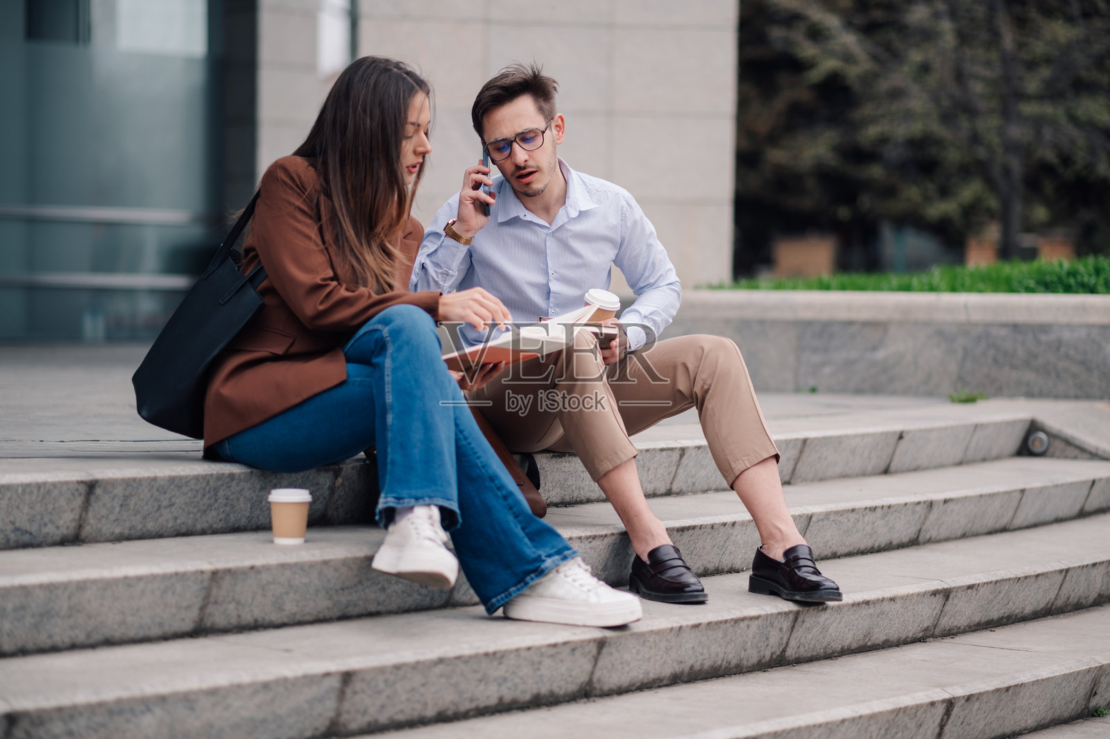 两位年轻专业人士在办公楼外的台阶上工作照片摄影图片