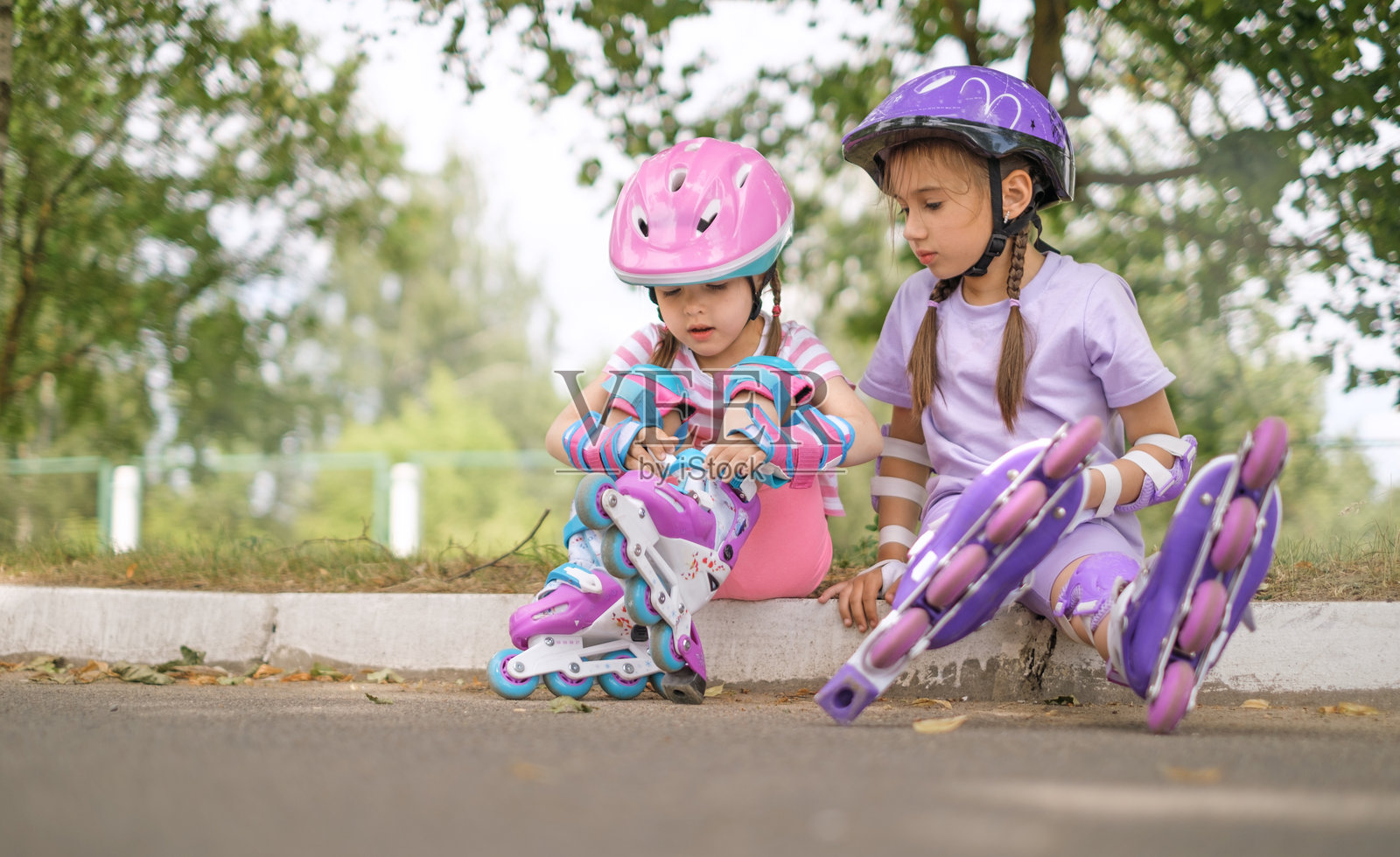 可爱的小女孩们坐在人行道上穿上轮滑鞋。夏季假期的活跃运动。照片摄影图片