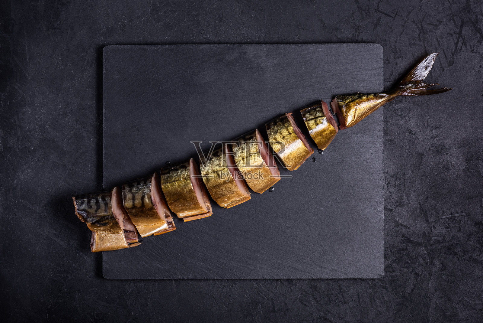 切片的冷熏鲭鱼去头，斜放在黑色背景的石质切菜板上。俯视图。海鲜概念，留有空白空间。照片摄影图片