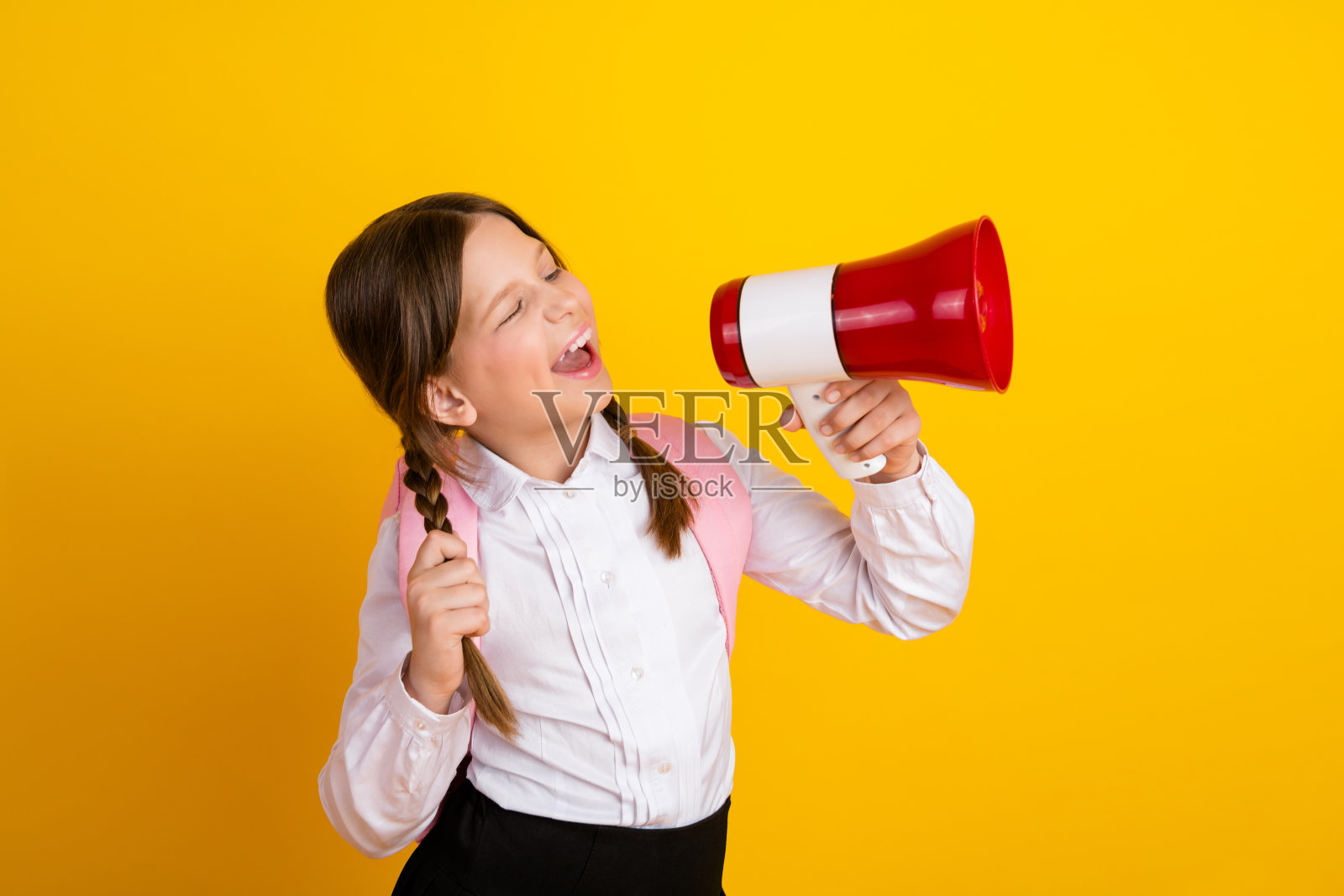 兴奋的快乐女学生手持扩音器，穿着白衬衫，背景为鲜艳的黄色。照片摄影图片