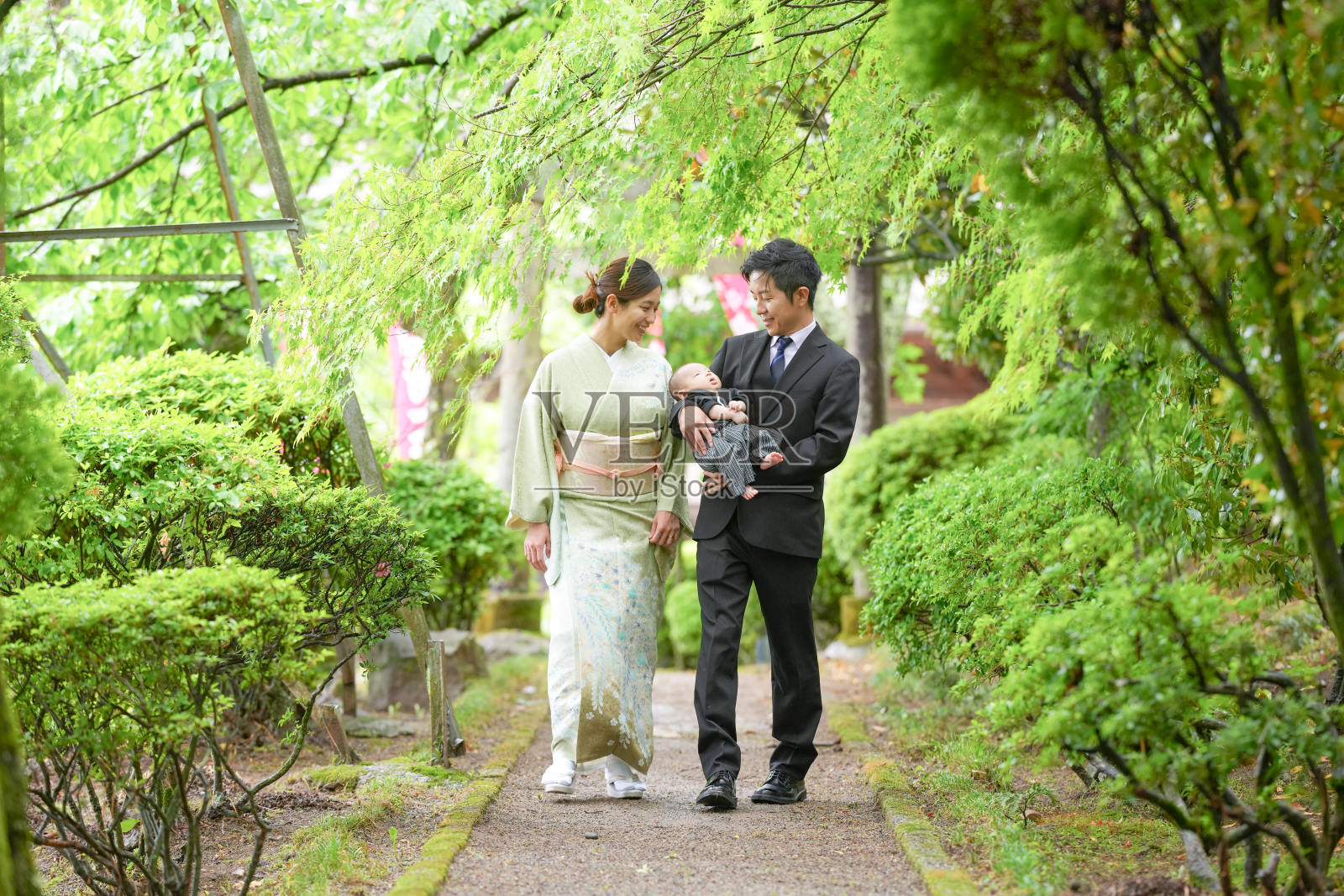 在五月的春天，一位穿着袴的一个月大的日本宝宝被一位西装男士抱着，和一位穿着和服的母亲一起散步，两人都是二十多岁，享受着温馨的家庭时光。照片摄影图片