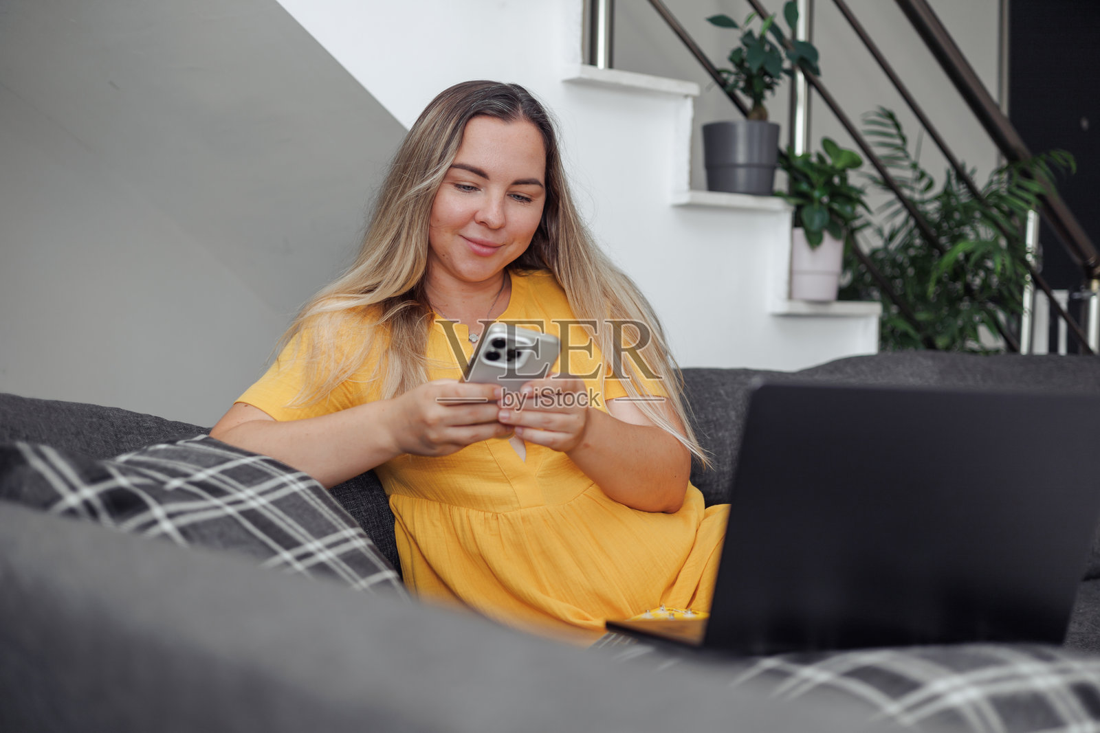 穿着黄色连衣裙的年轻女性在舒适的沙发上使用智能手机照片摄影图片