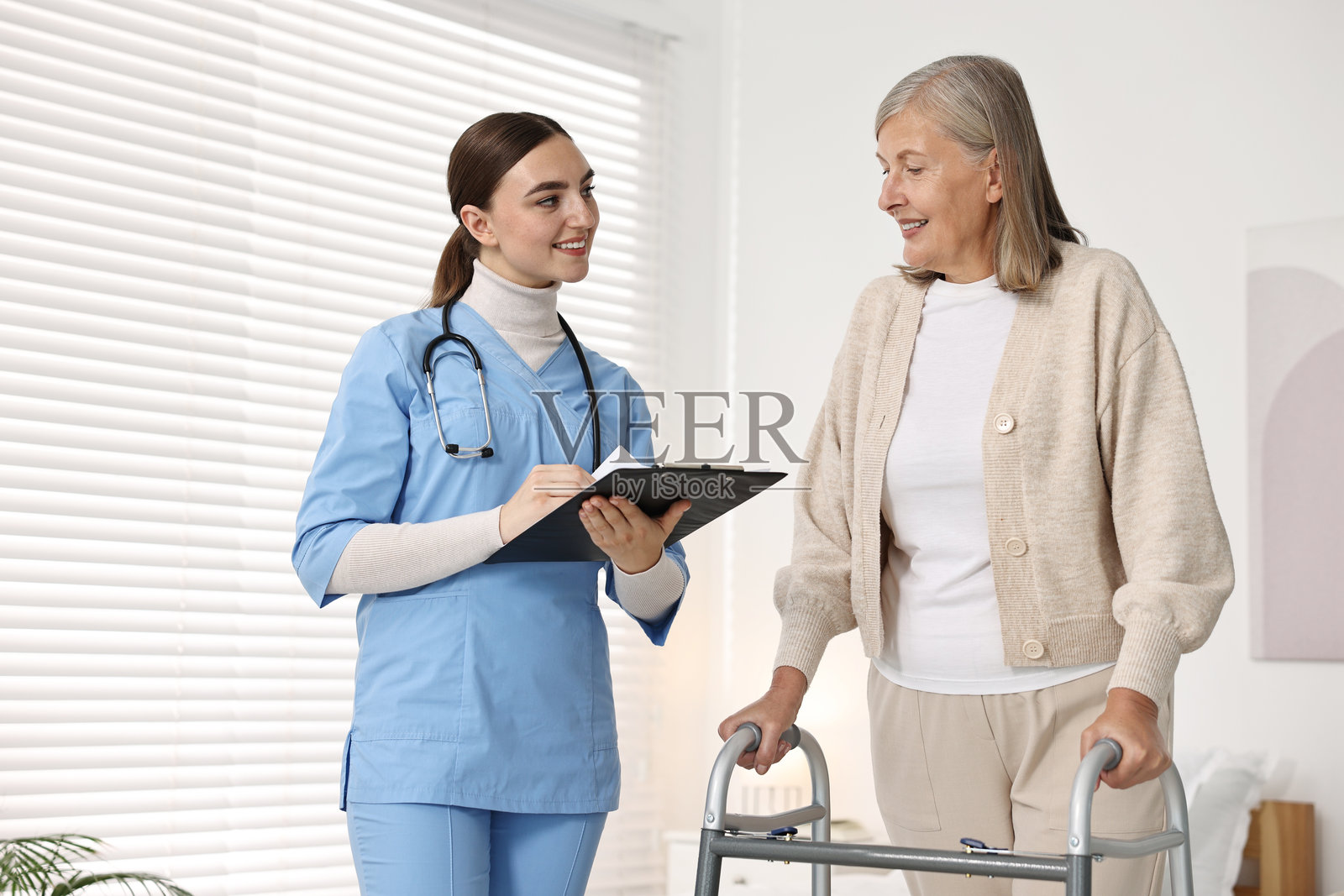 护士在诊所帮助使用助行器的老年女性照片摄影图片
