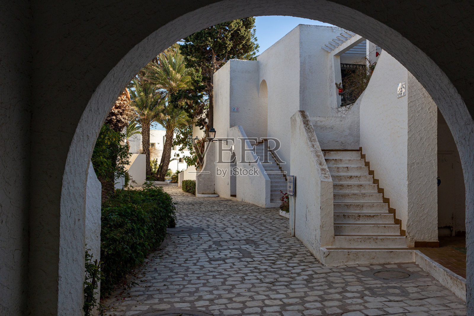 一条石头小径通向带有外部楼梯的白色建筑。照片摄影图片