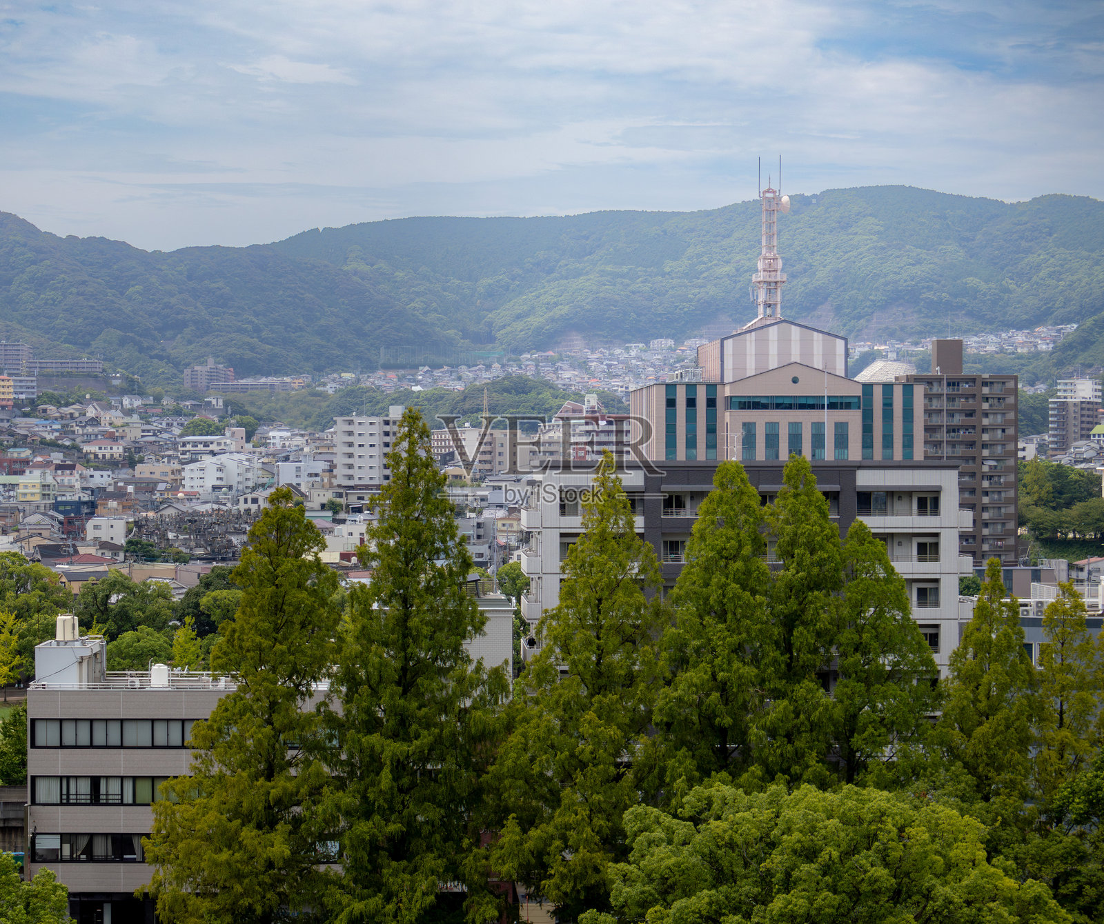 日本长崎市的建筑被郁郁葱葱的树木和山脉环绕。照片拍摄于阴天。照片摄影图片