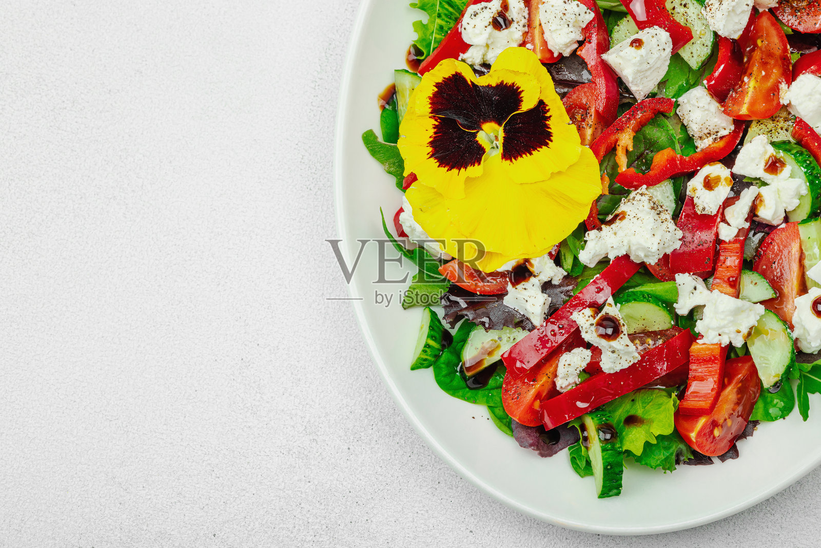 新鲜的素食沙拉，配有番茄、芝麻菜、山羊奶酪、橄榄和可食用花朵，盛放在白色盘子上照片摄影图片