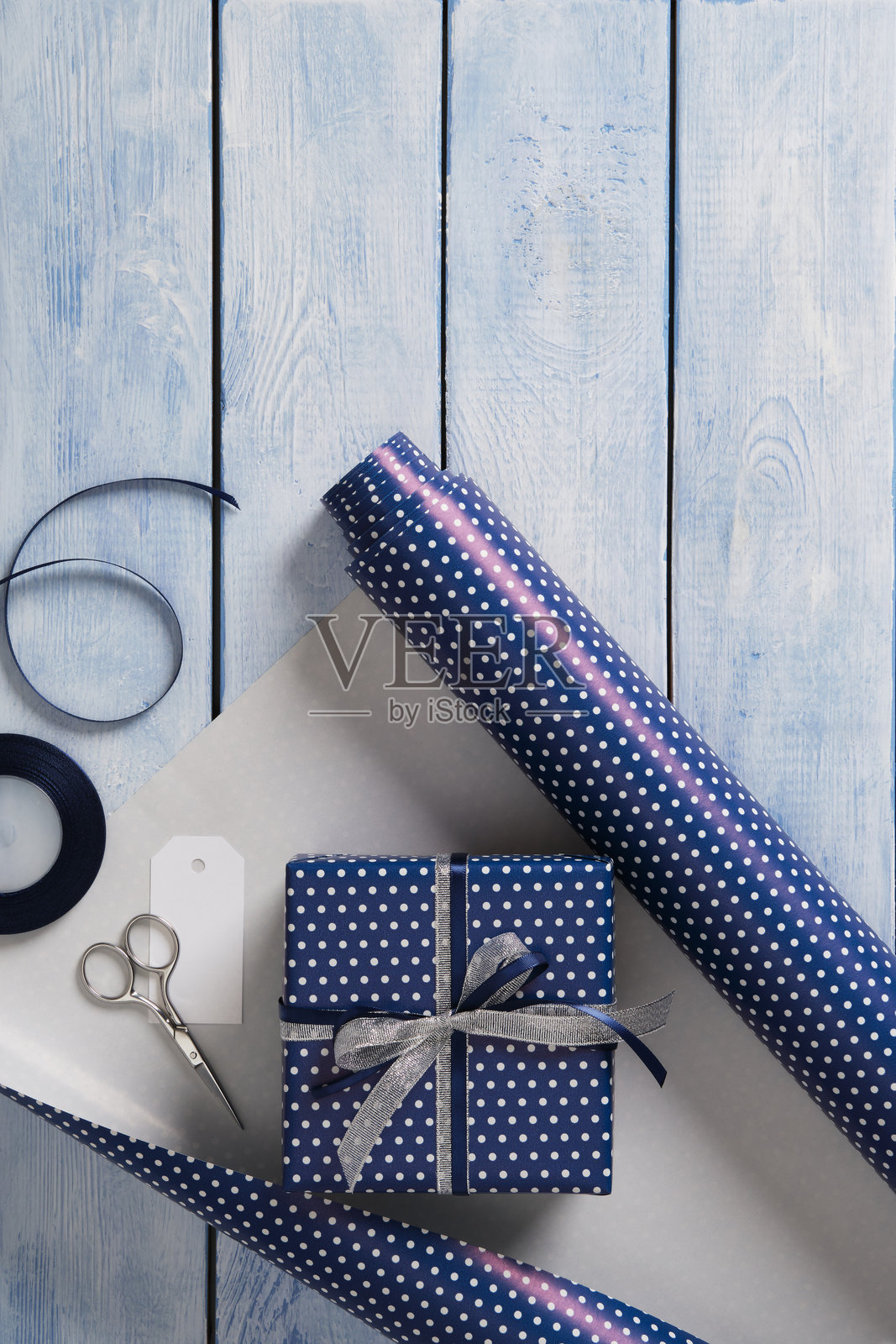 礼品包装用品。卷装包装纸、剪刀、丝带、已包装好的礼物。蓝色木质背景，留有您的文字空间。照片摄影图片
