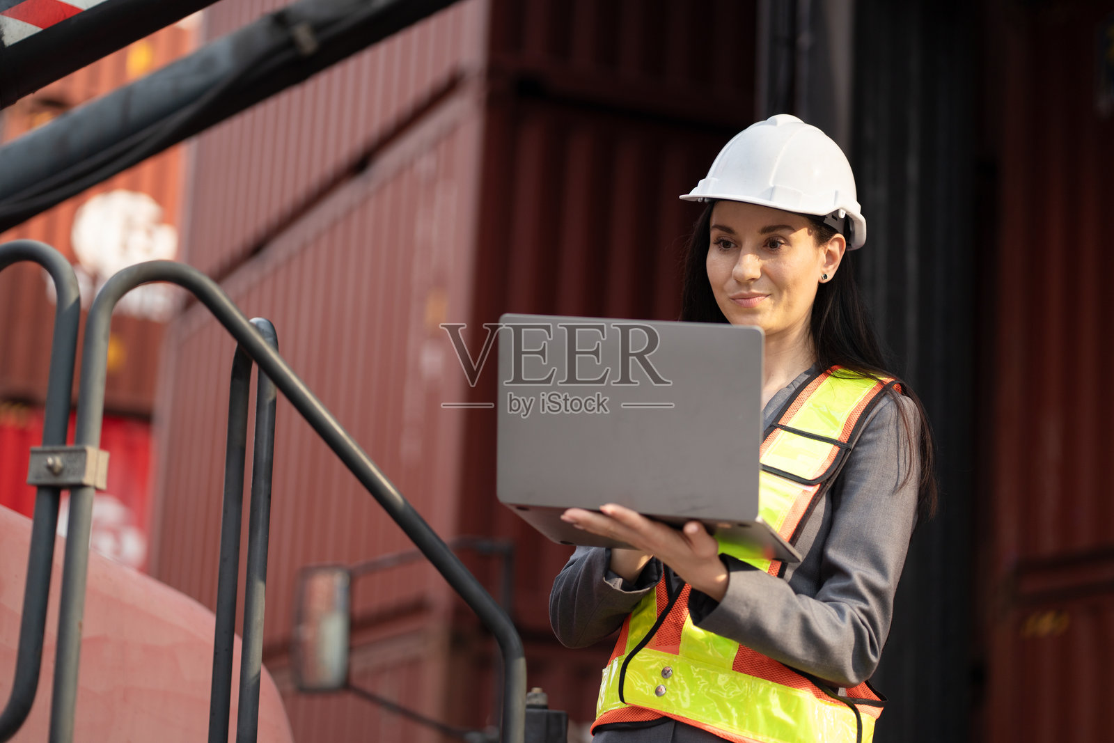 白人女性工程师在集装箱场地使用笔记本电脑与叉车工作照片摄影图片