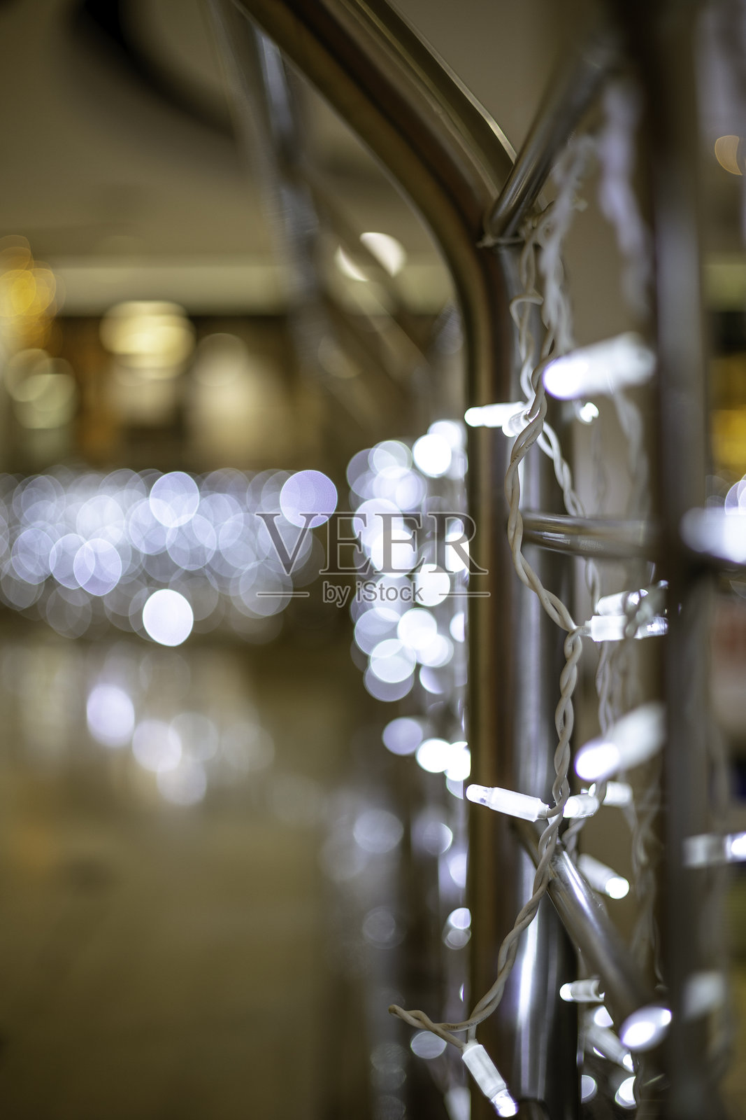 白色LED灯串紧绕在金属栏杆上，背景呈现模糊的散景效果。照片摄影图片