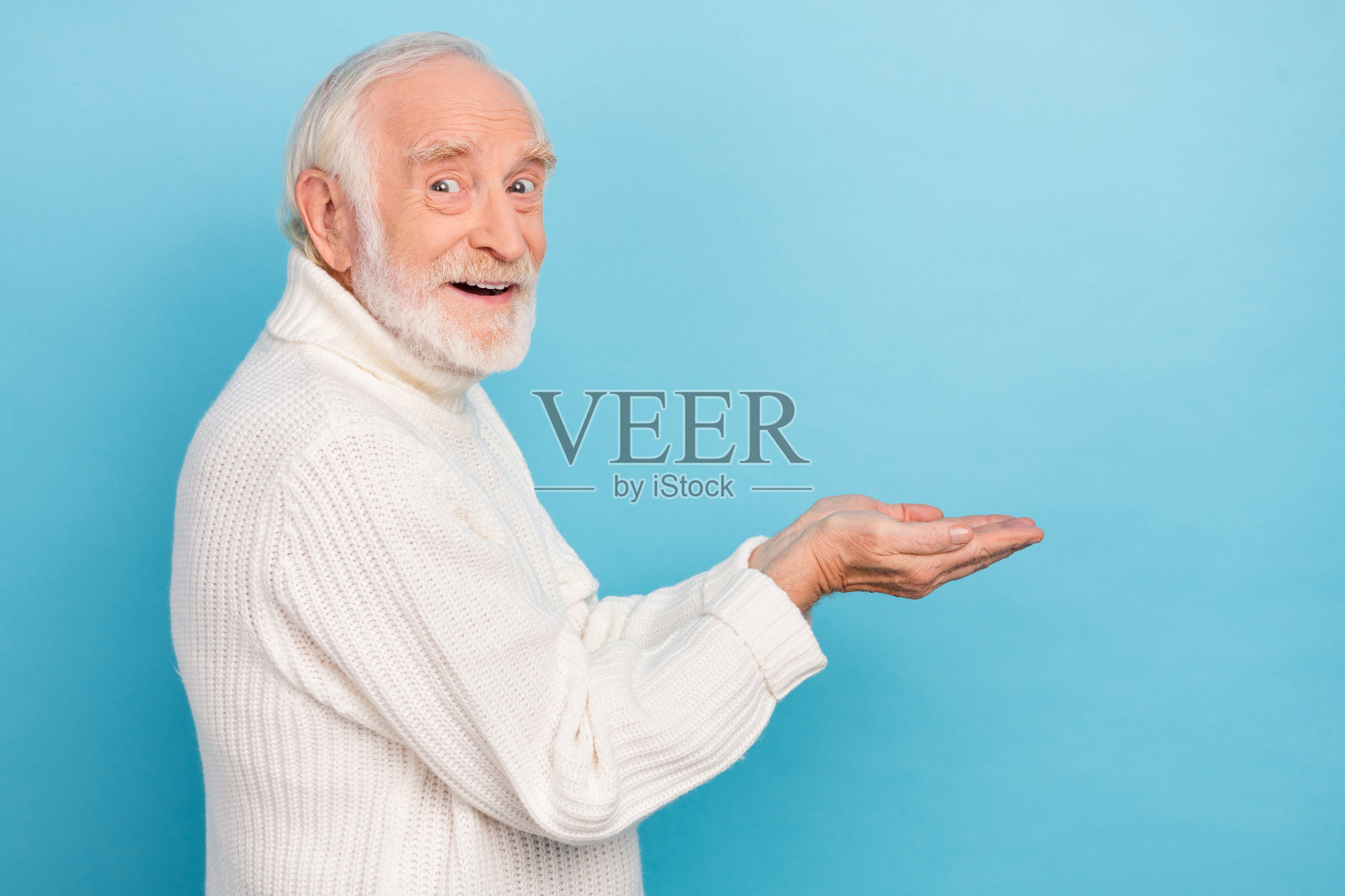 一位印象深刻的老年男子穿着白色毛衣，手持促销品，背景为蓝色。照片摄影图片