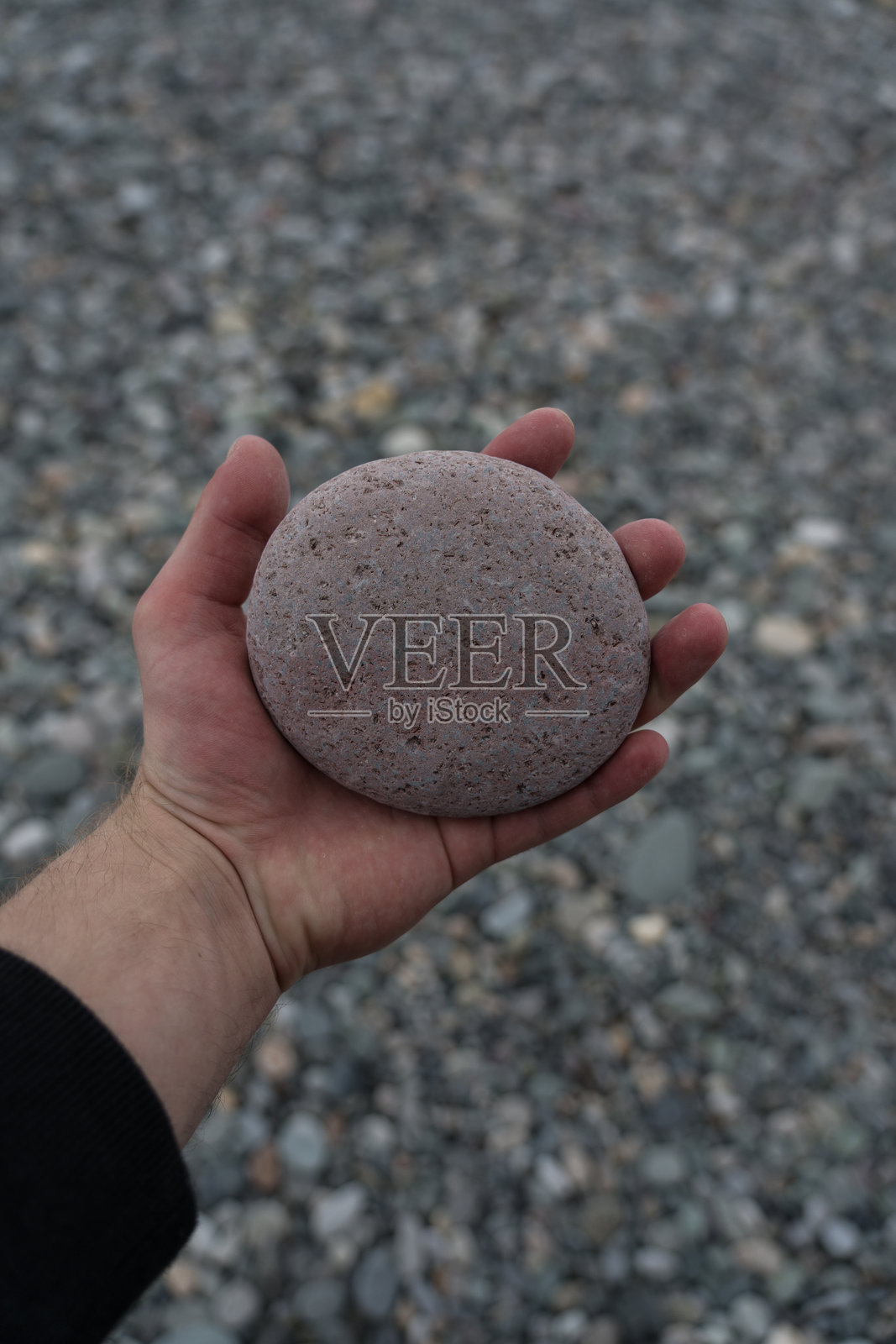 一个男人手中握着圆石，背景是石滩。照片摄影图片