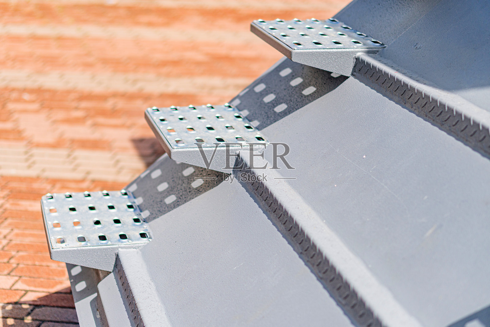 几种带孔的金属支架特写，背景为红砖瓦，附着在户外结构或设备上，用于安装目的。照片摄影图片