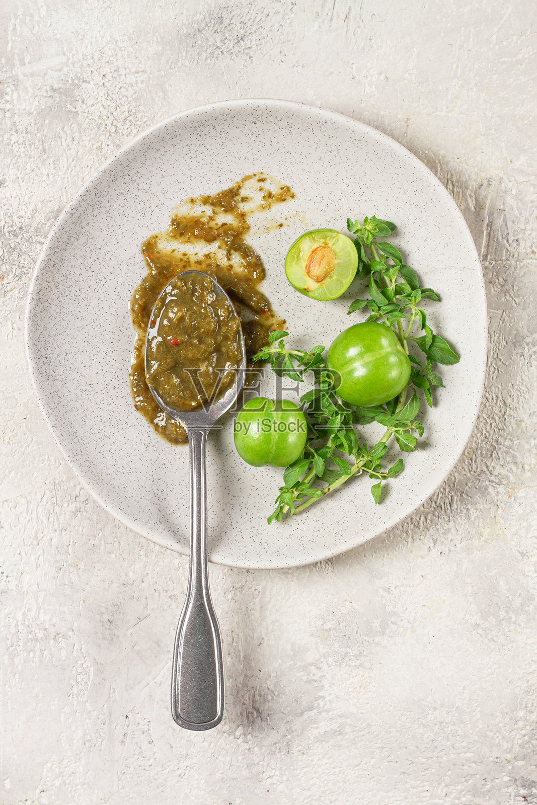 一把勺子盛着特克马利酱，放在盘子上，旁边有樱桃梅和薄荷，俯视图，无人。照片摄影图片