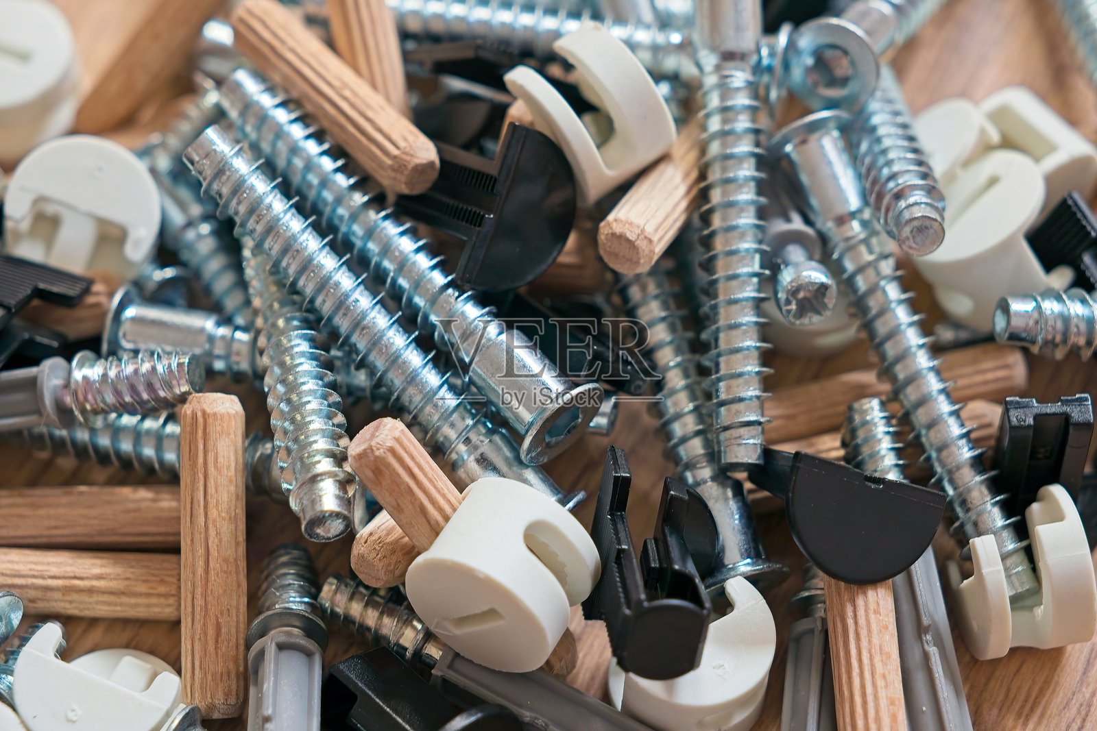 家具组装硬件特写，展示多种金属紧固件、木榫和散落在表面上的卡扣，突显精密制造组件。照片摄影图片