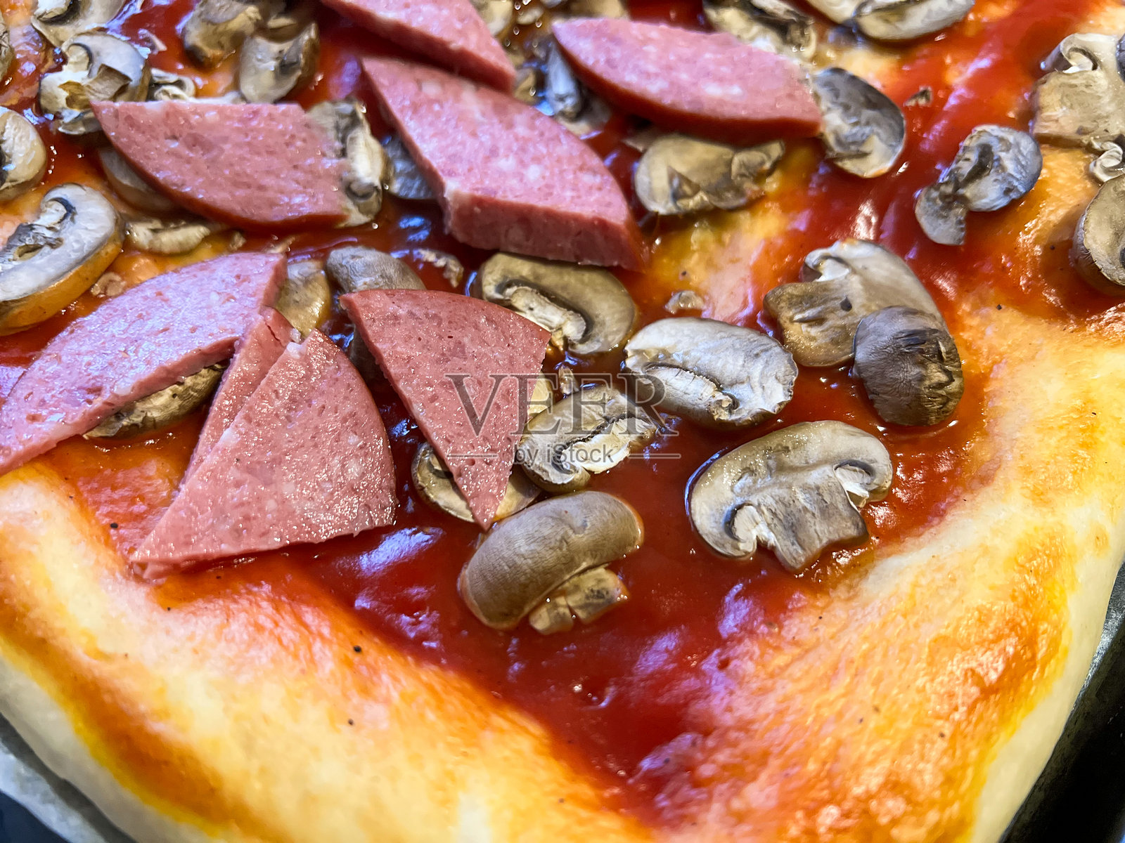 生的比萨饼，上面有番茄、蘑菇和香肠，等待烹饪。照片摄影图片