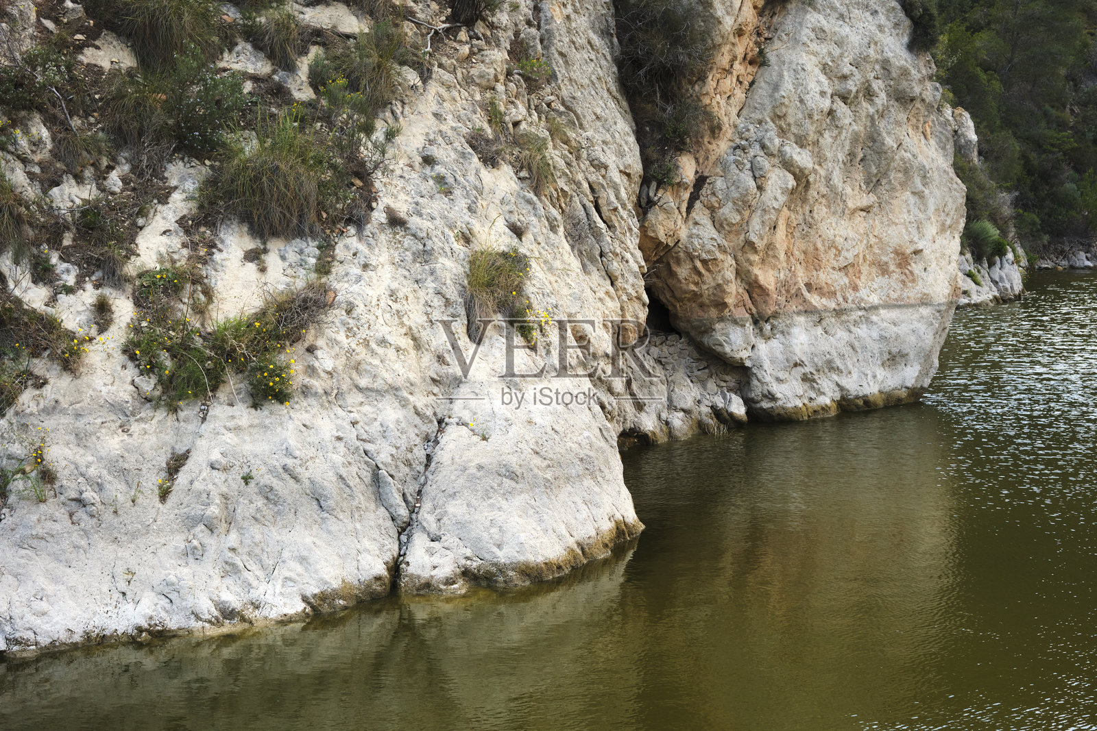 宁静湖泊旁的自然岩石悬崖形成，周围绿植繁茂照片摄影图片