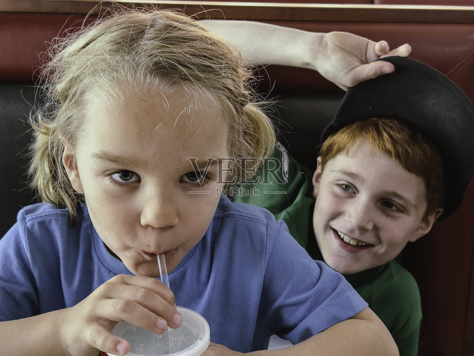 五岁金发男孩在南费城的餐馆用吸管喝饮料，九岁红发哥哥在旁边抢镜。照片摄影图片