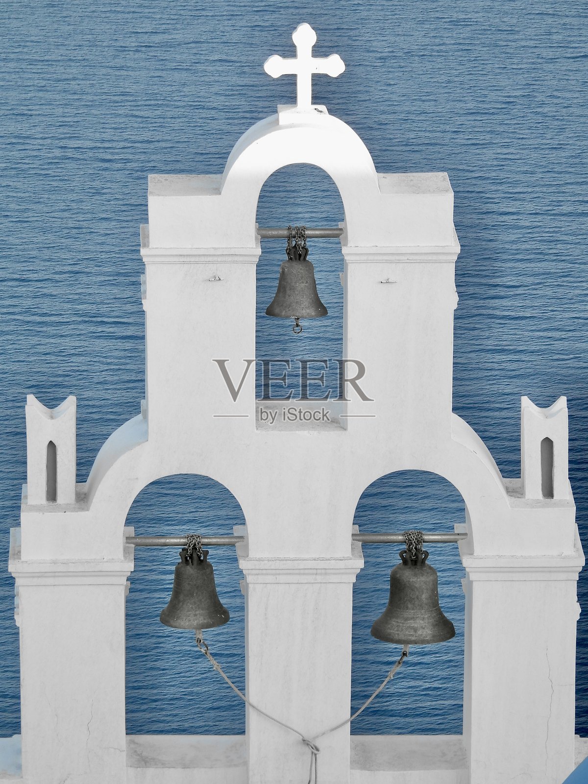 圣托里尼岛（希腊）一个星期三清晨，费拉的三口钟楼上方矗立着一个沐浴在阳光下的白色十字架。照片摄影图片