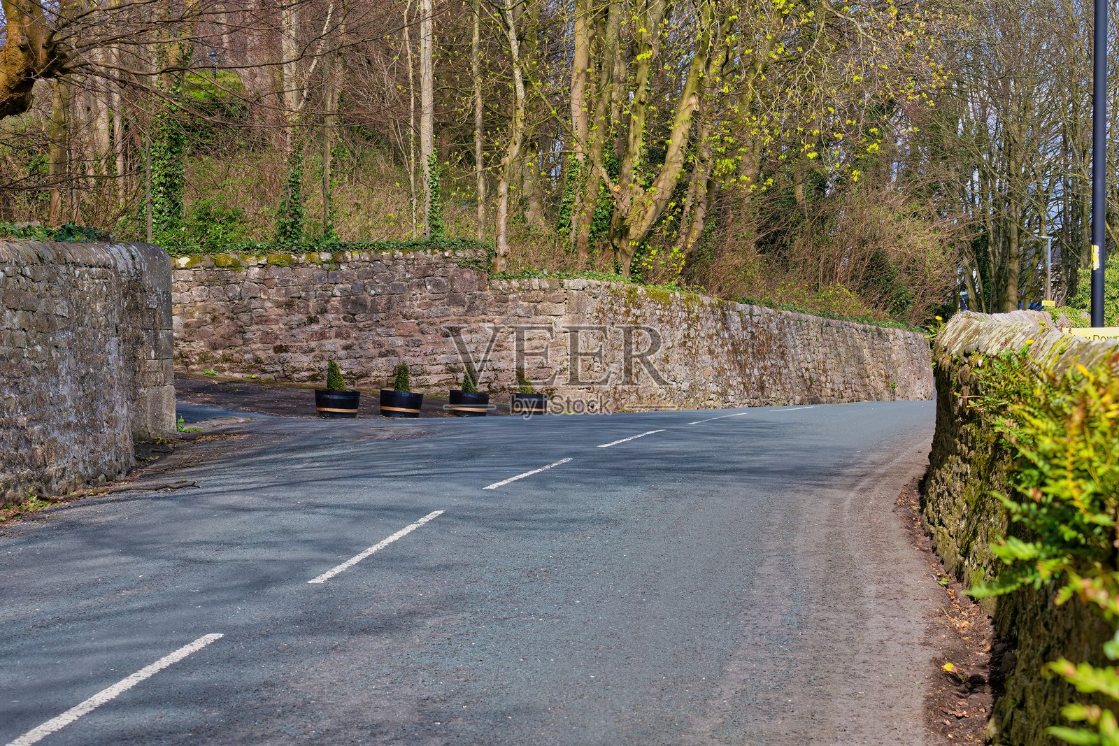 一条蜿蜒的道路两旁是石墙和绿树。照片摄影图片