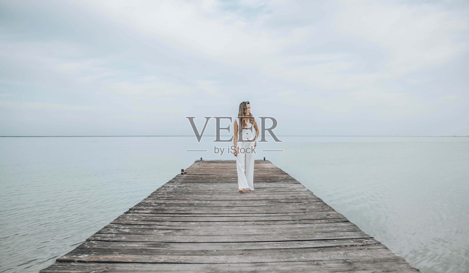 亚洲女性赤脚站在木栈道上，凝视着平静海平线的远方，身穿白色服装，沐浴在淡淡的云层下，正念，健康静修，旅行博客照片摄影图片