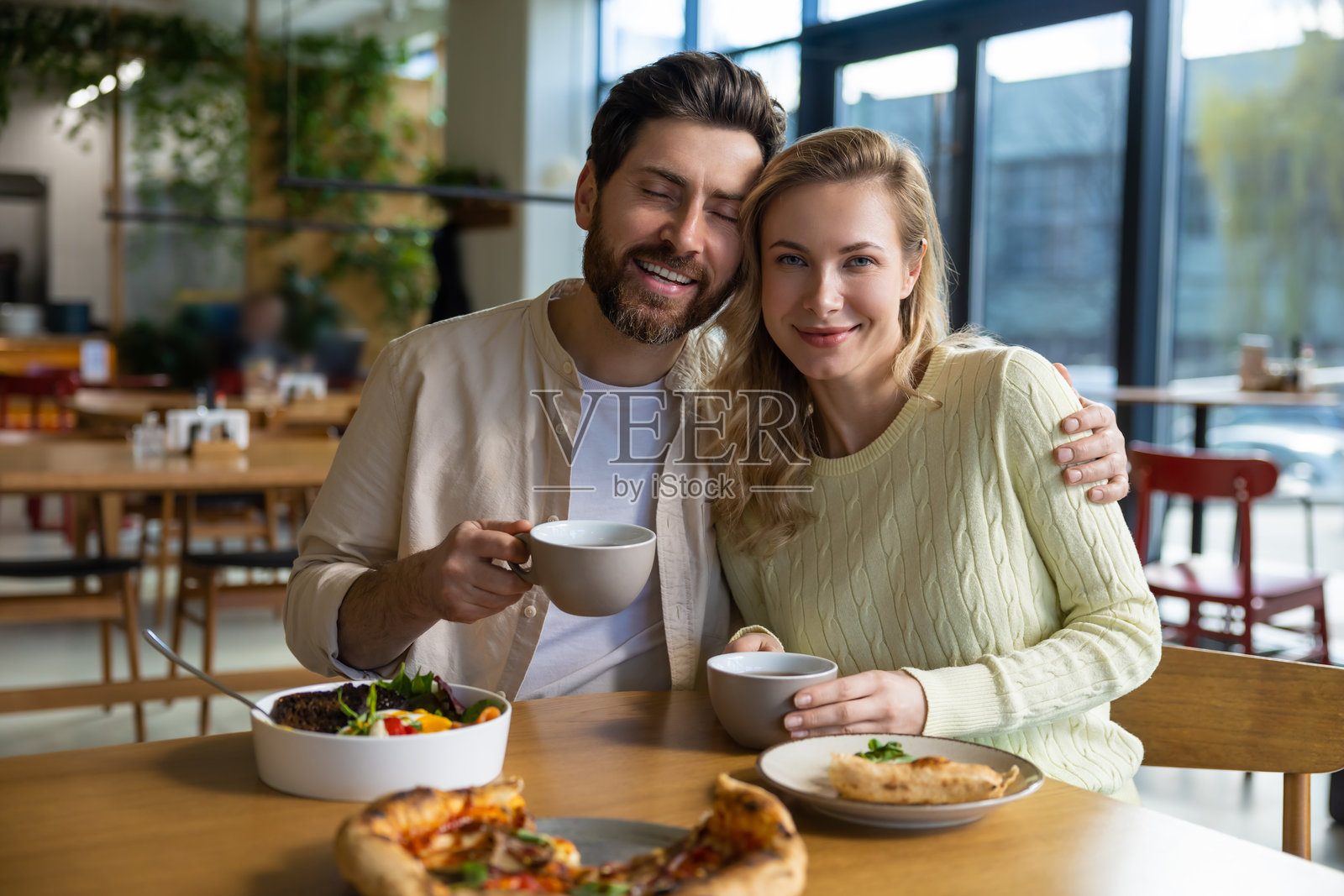 一对有胡子的男女在餐厅享用披萨和咖啡。照片摄影图片