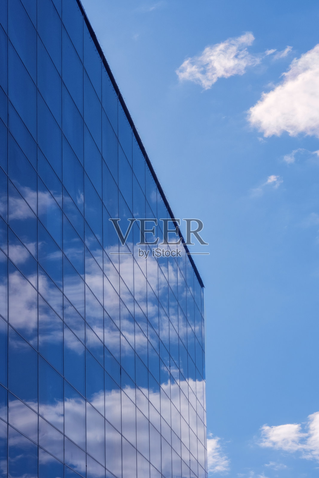 蓝天和白云倒映在高大现代建筑的玻璃墙上。背景。照片摄影图片