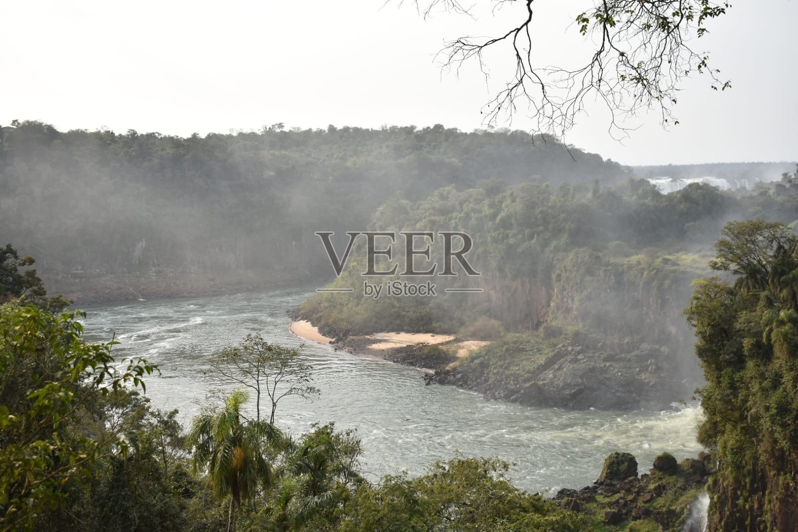伊瓜苏河在雾气弥漫的雨林中蜿蜒流向瀑布，阿根廷/巴西照片摄影图片