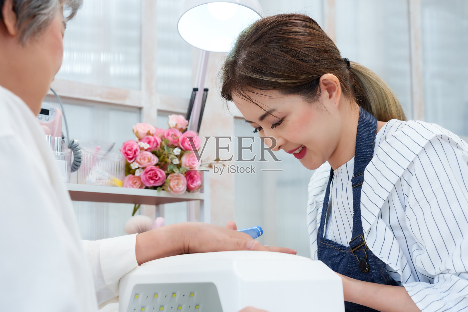 美甲师为一位年长的亚洲女性修指甲，营造舒适的美甲水疗体验，倡导美容、护理、健康、卫生、放松的生活方式，体现小型专业企业的客户关怀服务。照片摄影图片