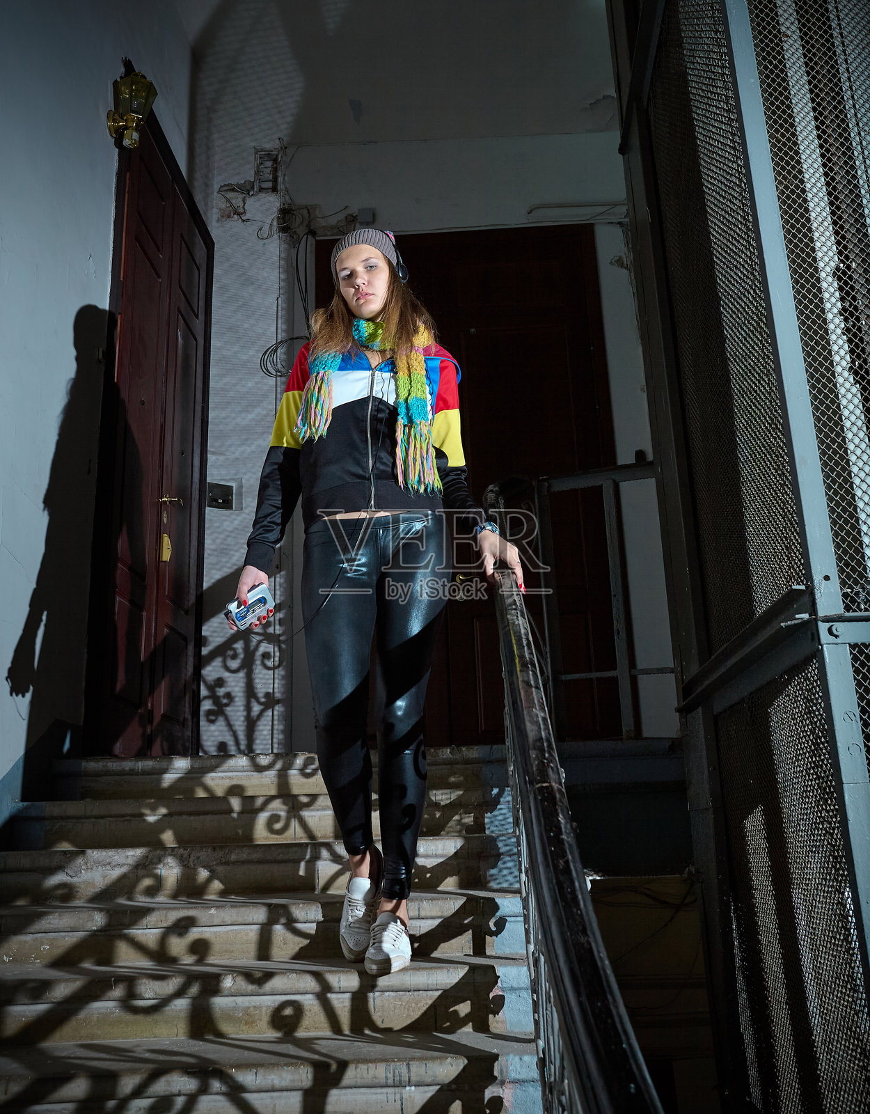 穿着90年代服装的迷人年轻女性走下旧楼梯，听着卡带播放器里的音乐照片摄影图片