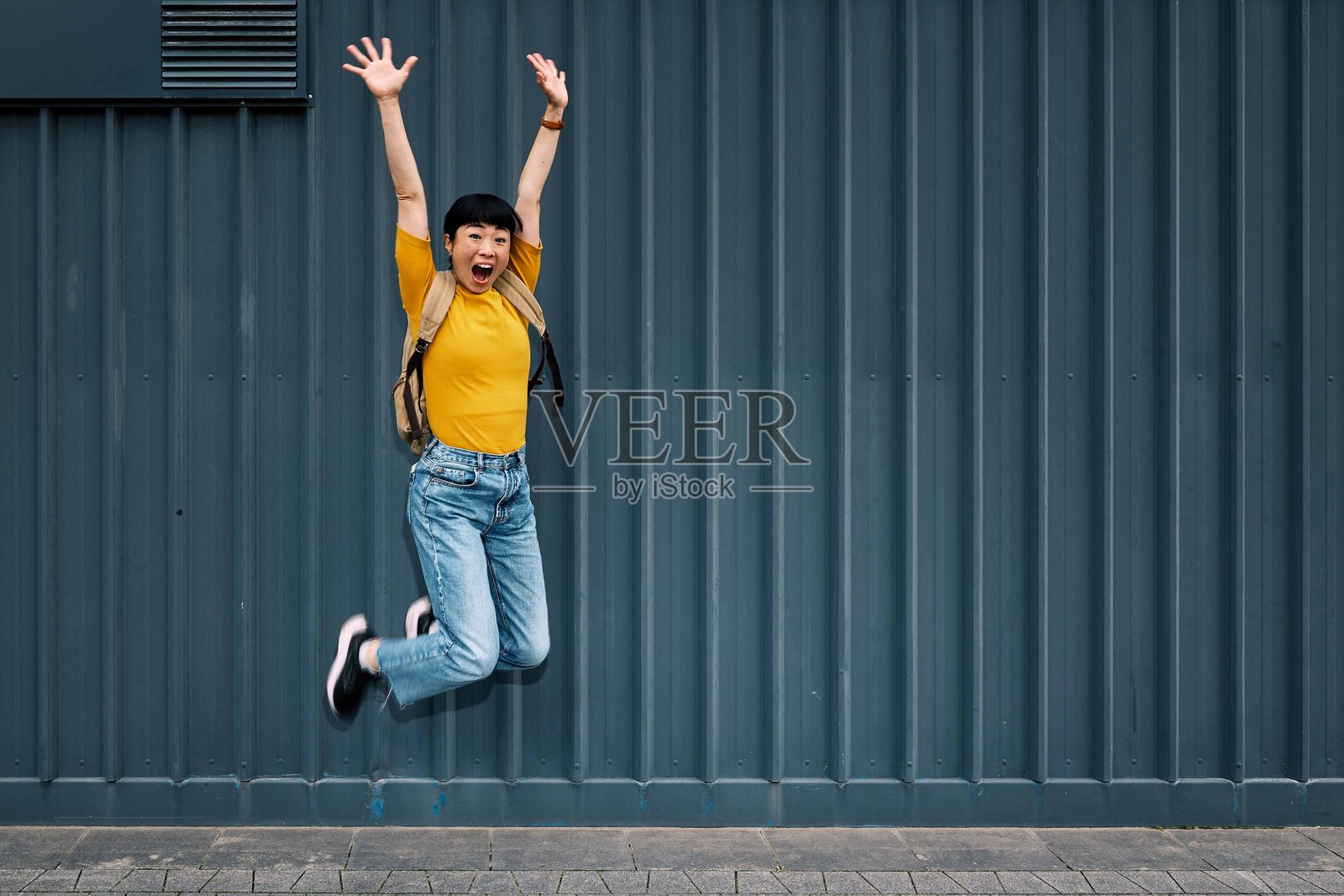 满怀喜悦的日本女性在城市街道上背着背包跳跃。照片摄影图片