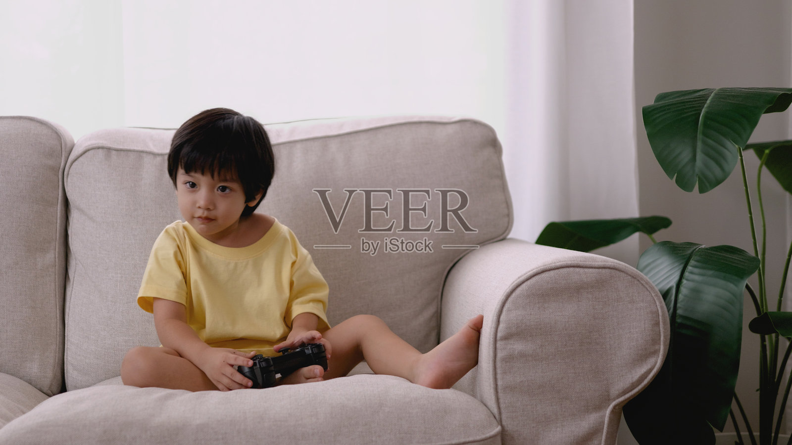 亚洲男孩在早晨的客厅里玩电子游戏，手握游戏手柄。照片摄影图片