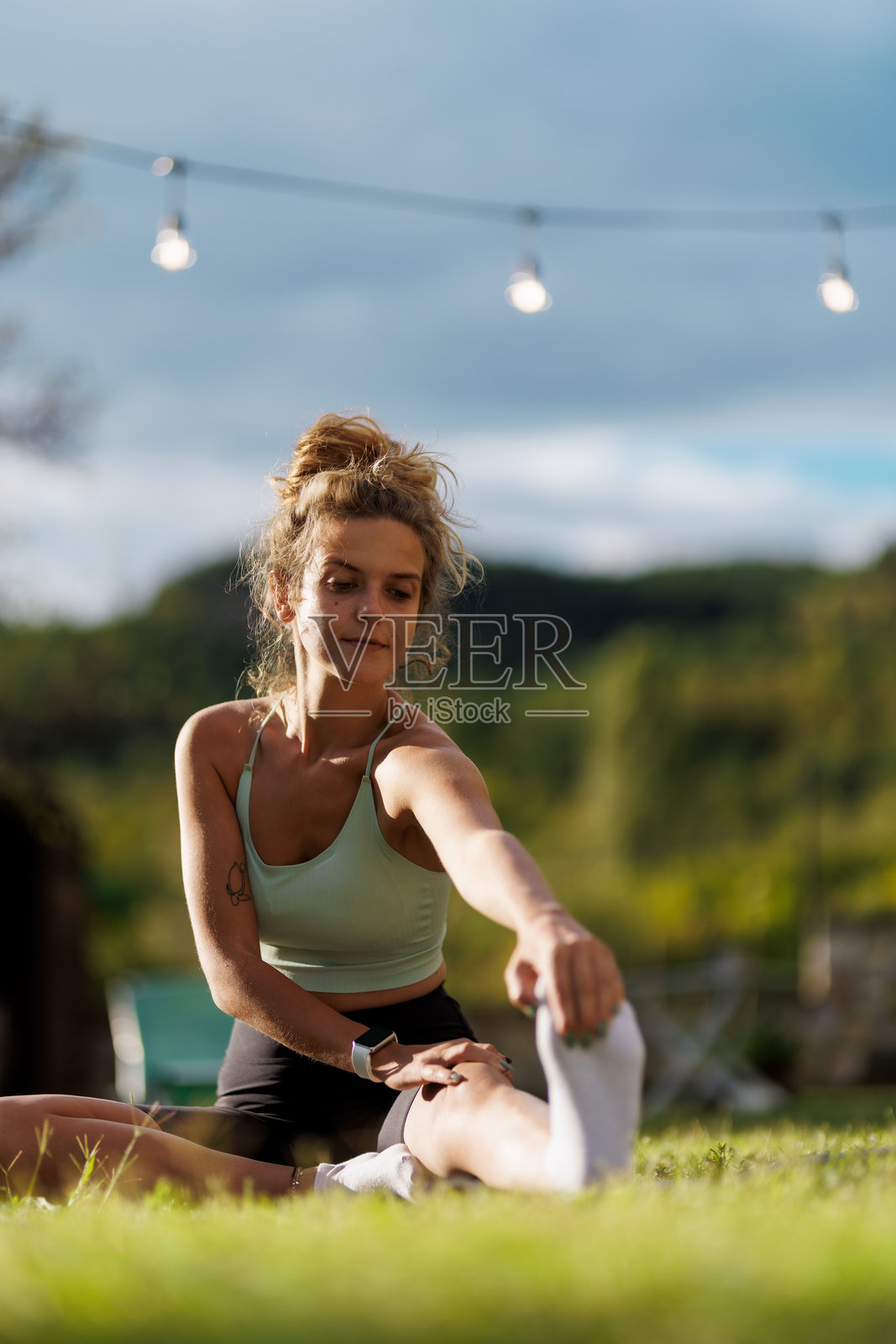 年轻女性在阳光明媚的日子里，在美丽的自然环境中，绳灯下伸展身体照片摄影图片