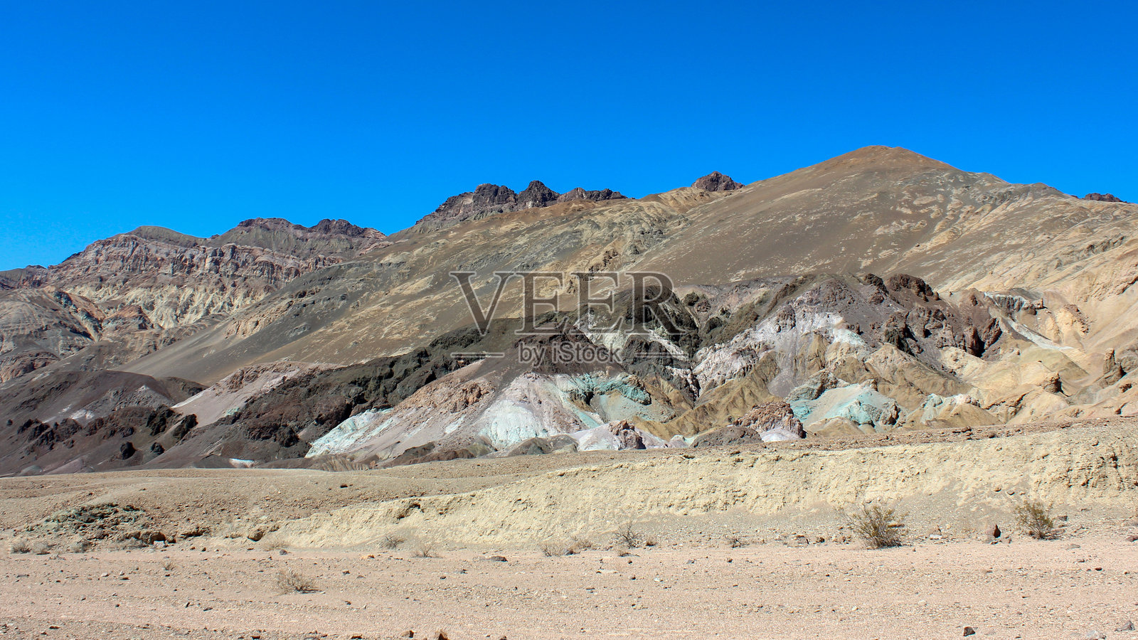 在清澈蓝天下，偏远沙漠景观中的山坡上色彩斑斓的矿物形成。照片摄影图片
