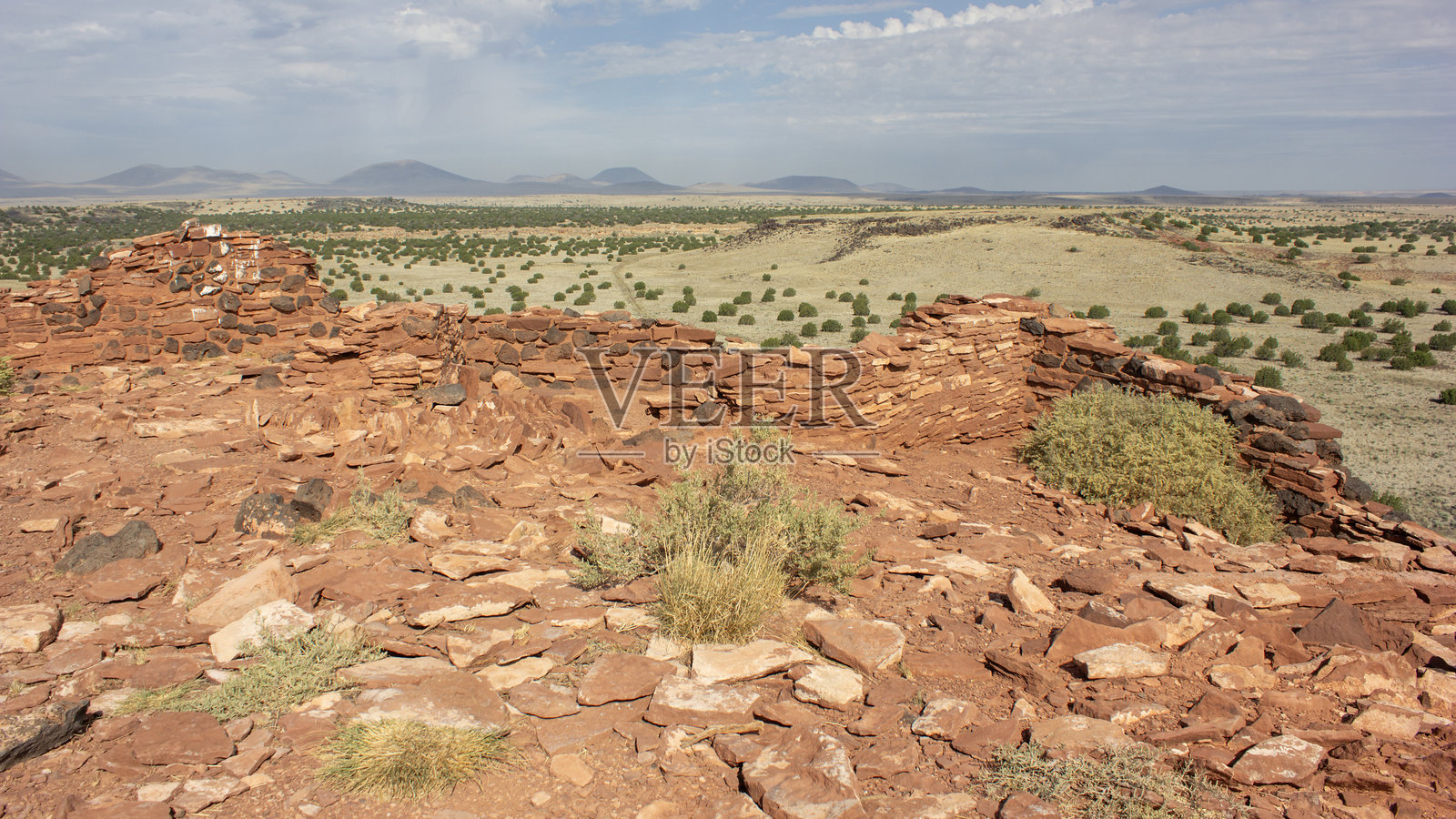 古老的石头遗迹位于山丘上，俯瞰着广阔的干旱景观和远处的山脉，在明亮的白天中显得格外清晰。照片摄影图片
