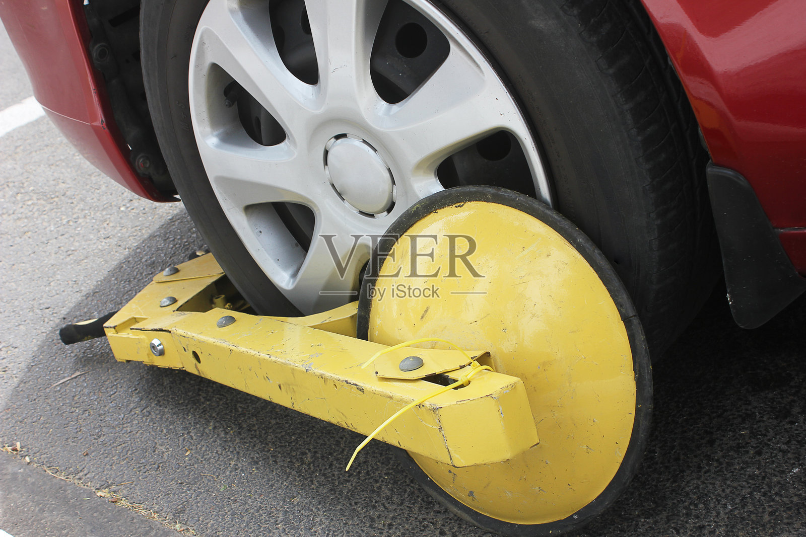 一辆停着的汽车，轮胎上有一个黄色的锁具，因非法停车而被锁。轮胎锁在禁止停车的区域。经过情绪化编辑的图片，具有哑光效果和浅景深。照片摄影图片