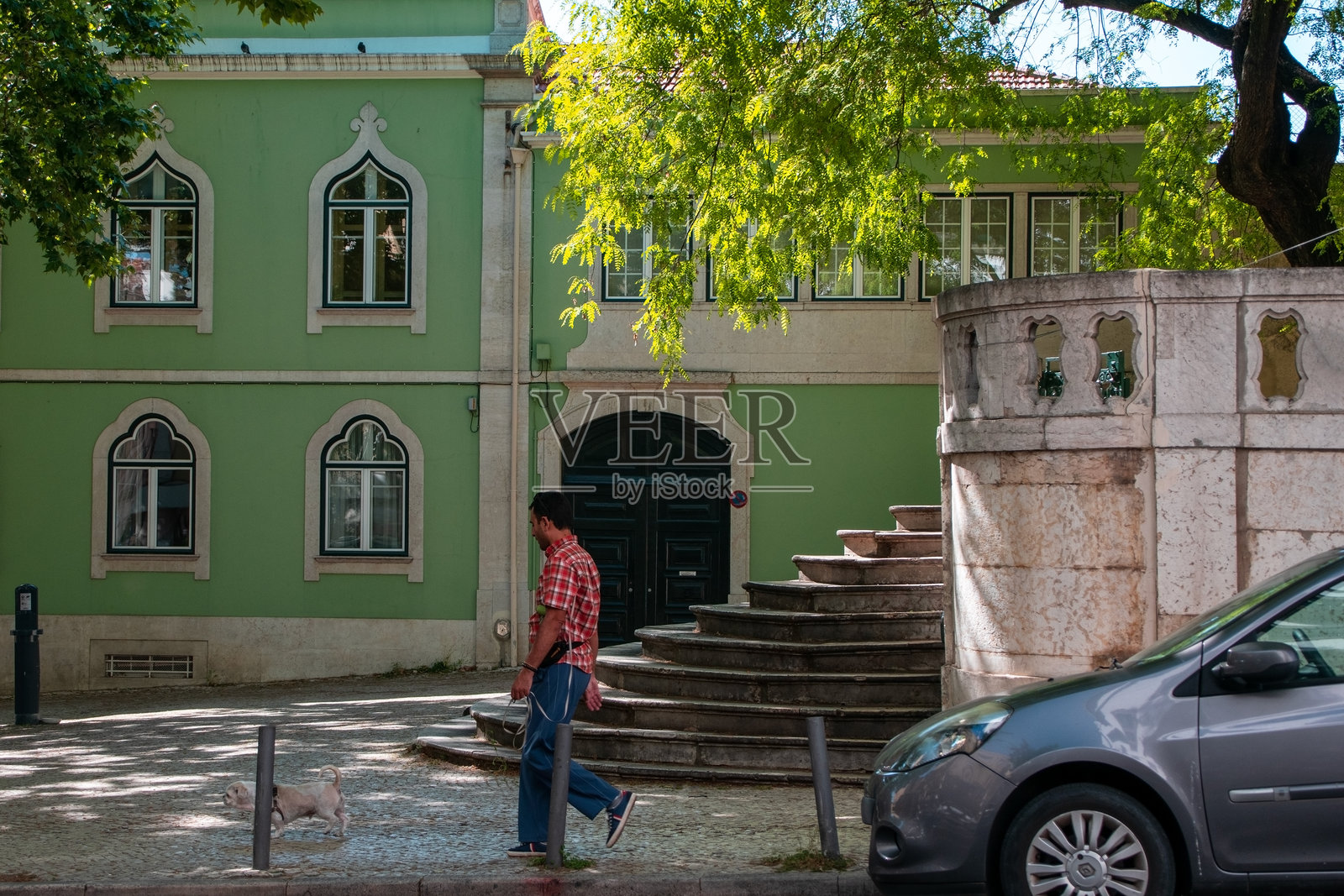 男子在一座有楼梯的绿色建筑前遛狗照片摄影图片