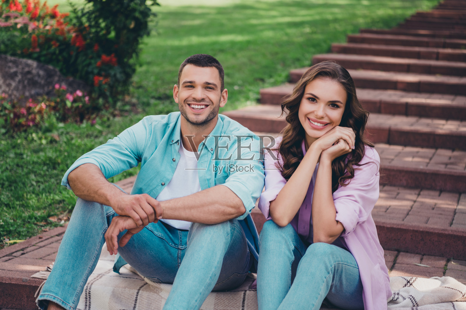 可爱的梦幻情侣穿着休闲服装，在户外花园的台阶上走动和坐着，享受阳光明媚的天气。照片摄影图片