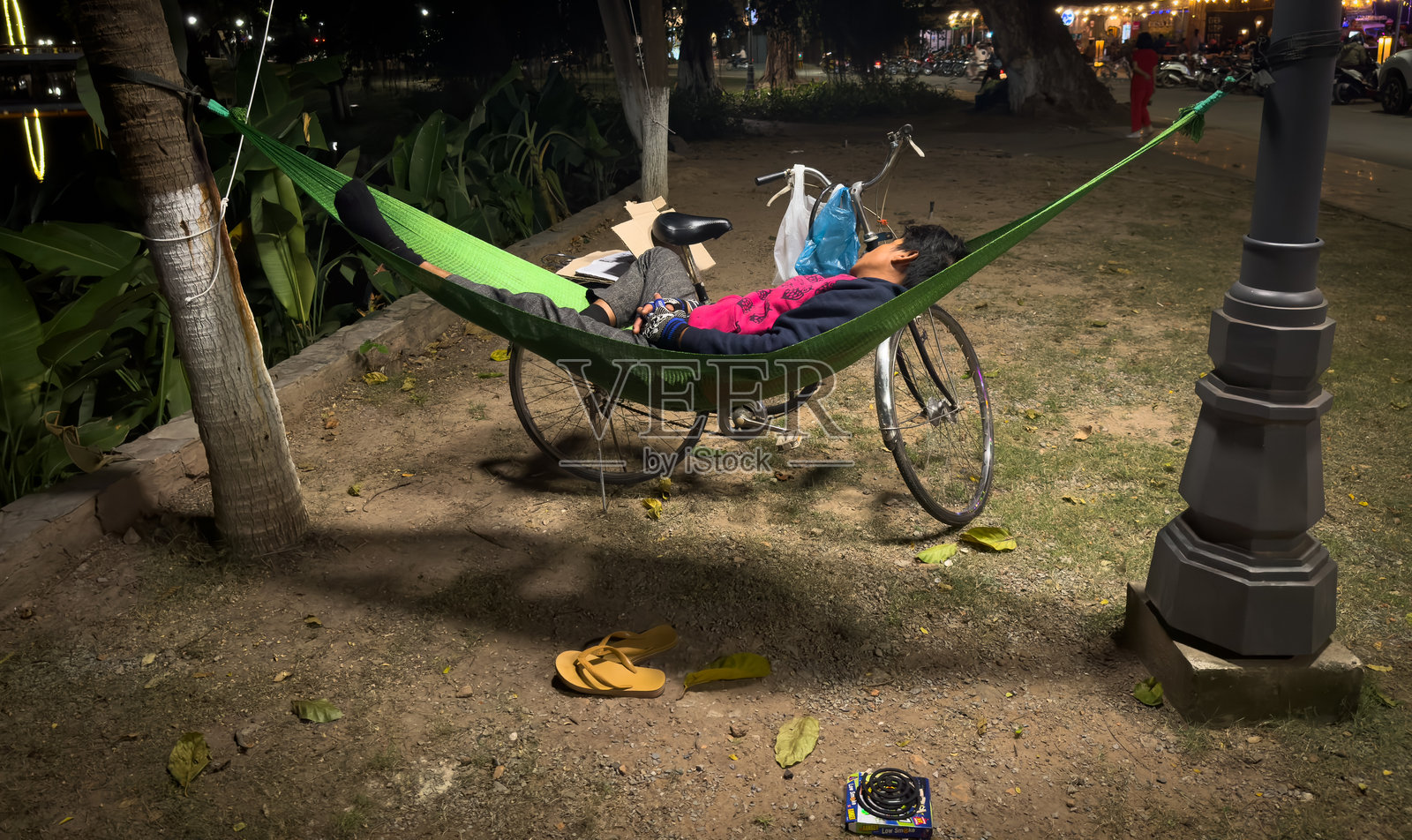 一个男人在柬埔寨暹粒的暹粒河旁的吊床上睡觉，身边放着他的自行车。照片摄影图片
