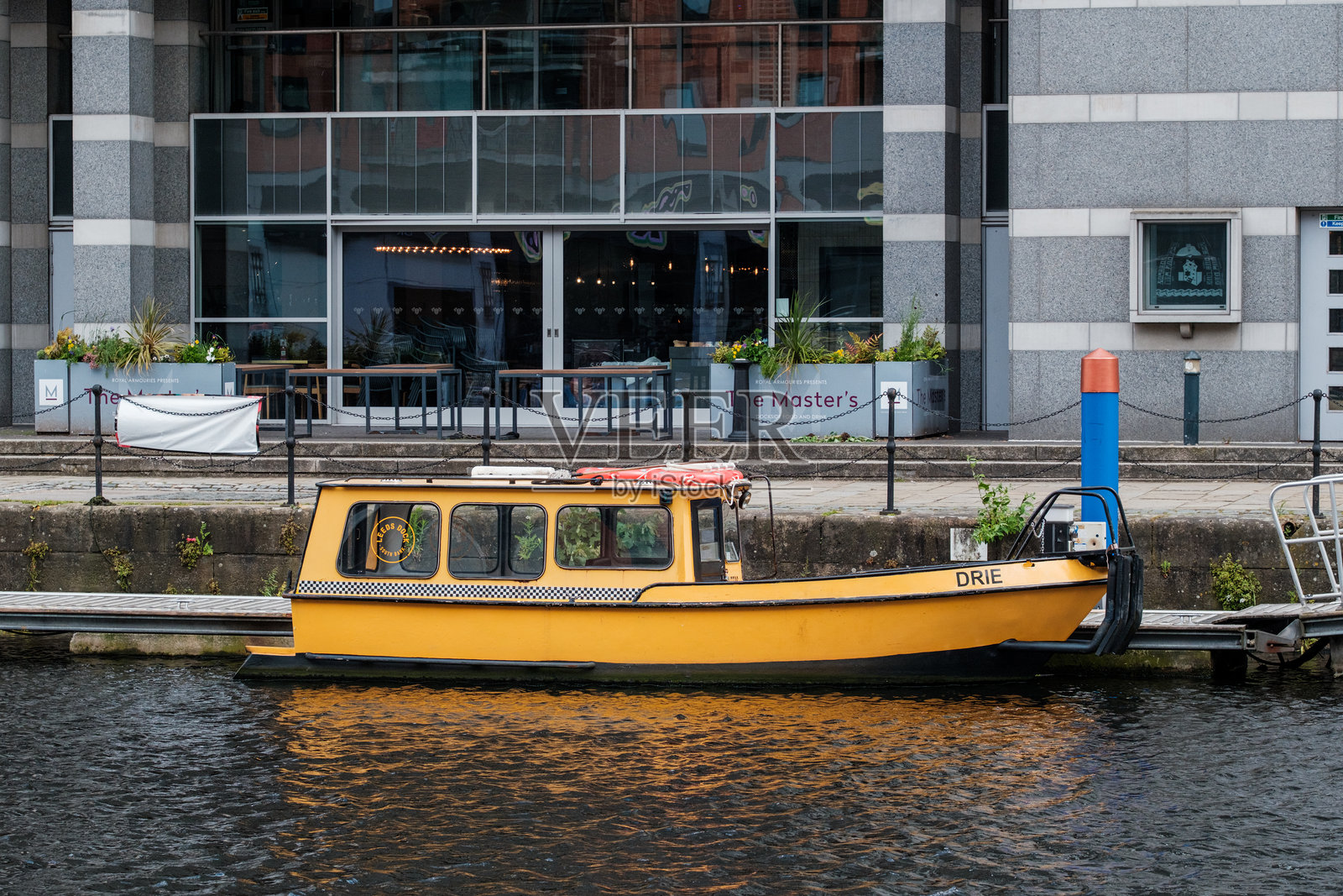 一艘明亮的黄色水上出租车停靠在利兹运河旁,周围是现代建筑。照片摄影图片