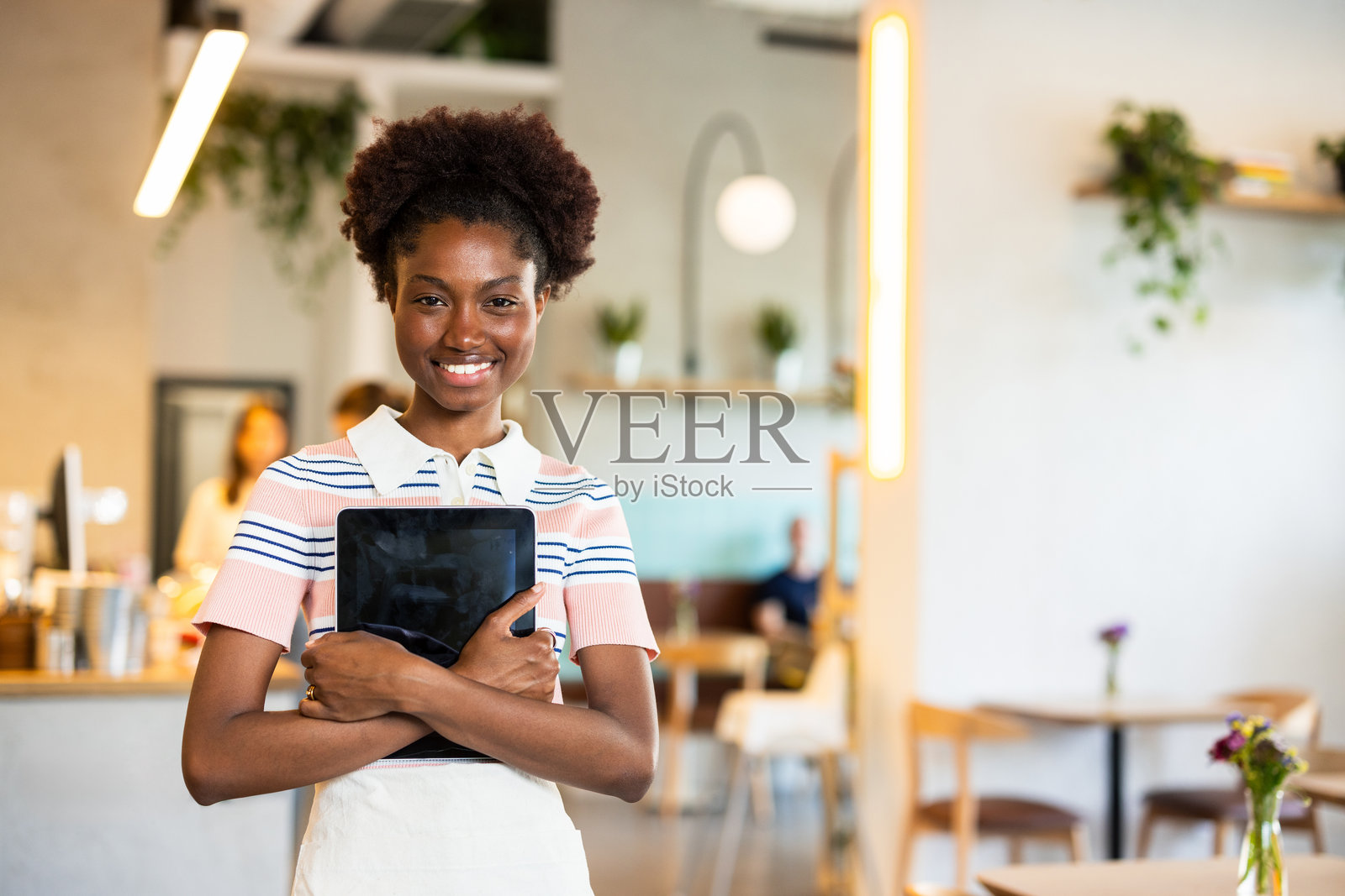 年轻女服务员在餐厅里微笑着手持数字平板电脑对着镜头。照片摄影图片