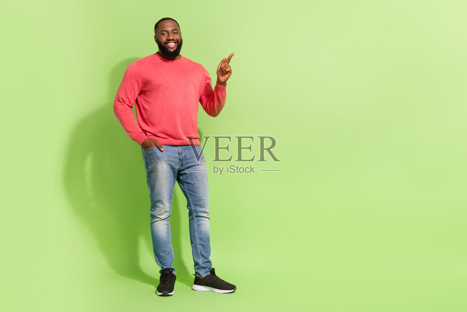全身肖像的快乐男人，手插口袋，手指指向空白区域，背景为绿色。照片摄影图片
