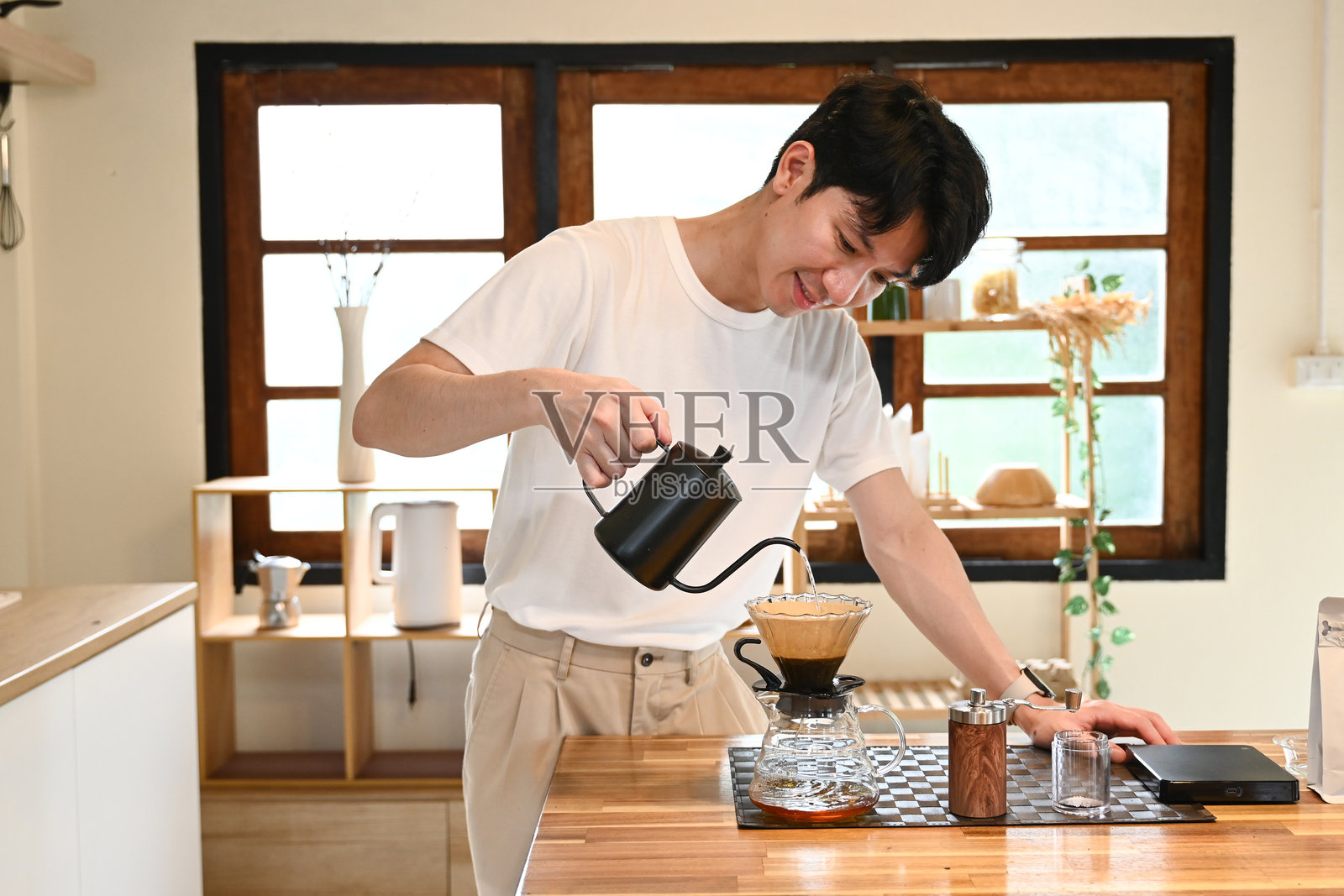 一个男人正在把咖啡倒入杯子里。咖啡是从一个黑色的咖啡壶中倒出来的。男人在倒咖啡时面带微笑。照片摄影图片