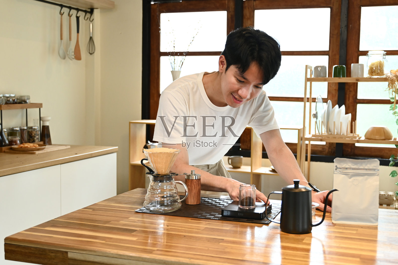 一个男人在厨房里煮咖啡。他面带微笑，享受这个过程。照片摄影图片