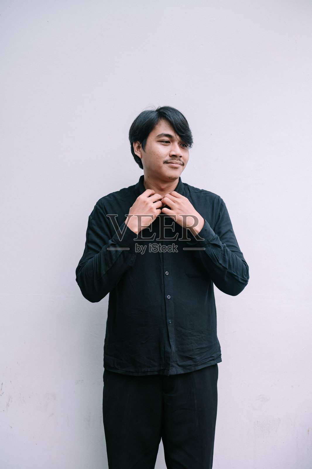 身穿黑色衬衫的年轻男子在中性背景前沉思照片摄影图片