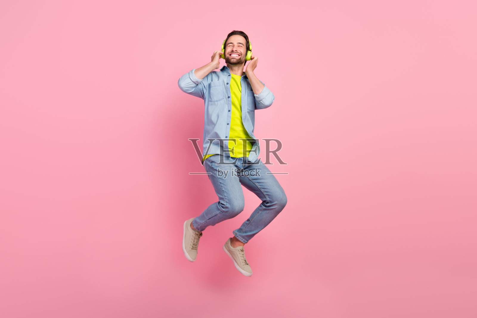 全身照，年轻兴奋的男士戴着耳机享受收音机，穿着毛衣，背景为粉色。照片摄影图片