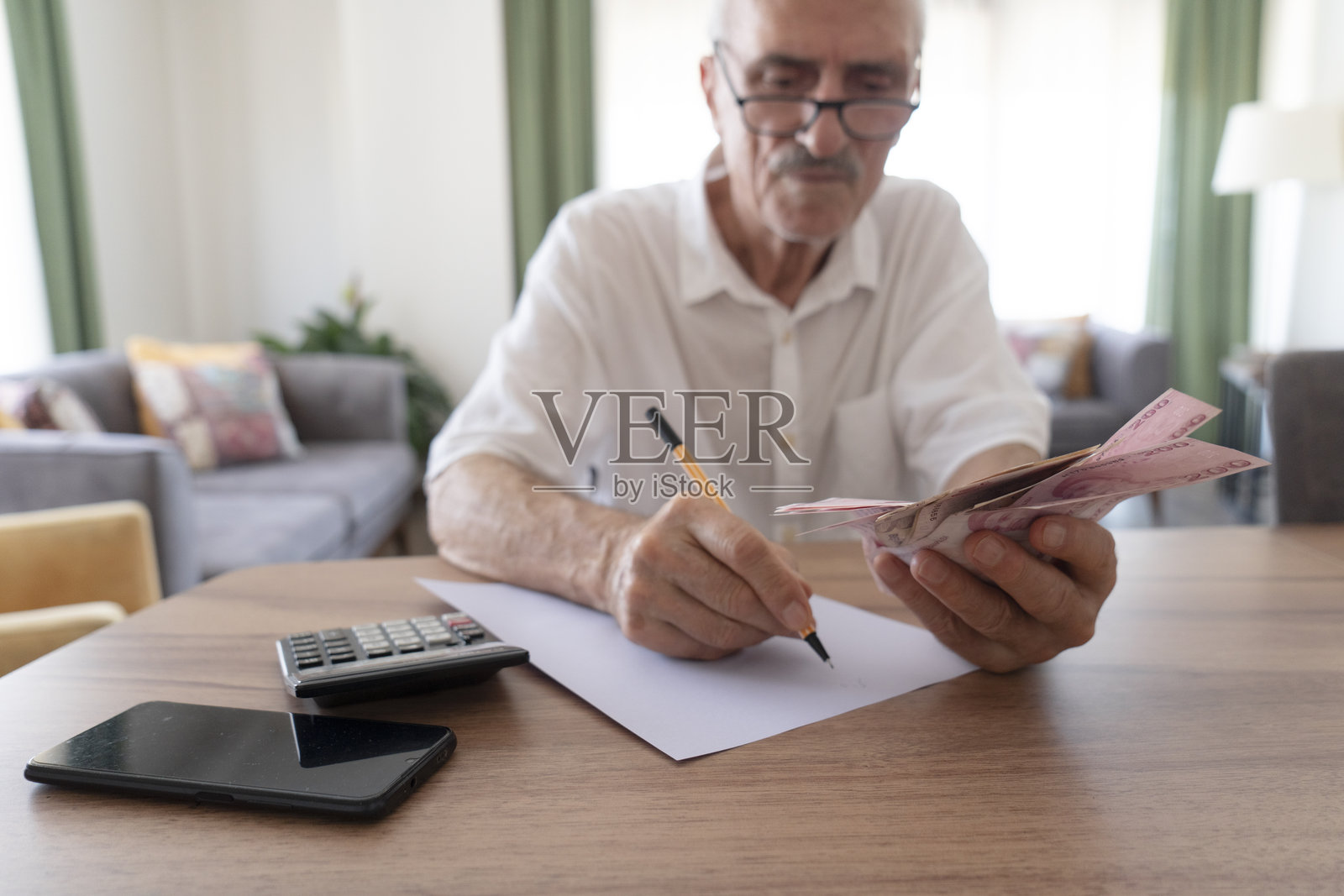老年男子在家中管理财务，手握现金并使用计算器照片摄影图片