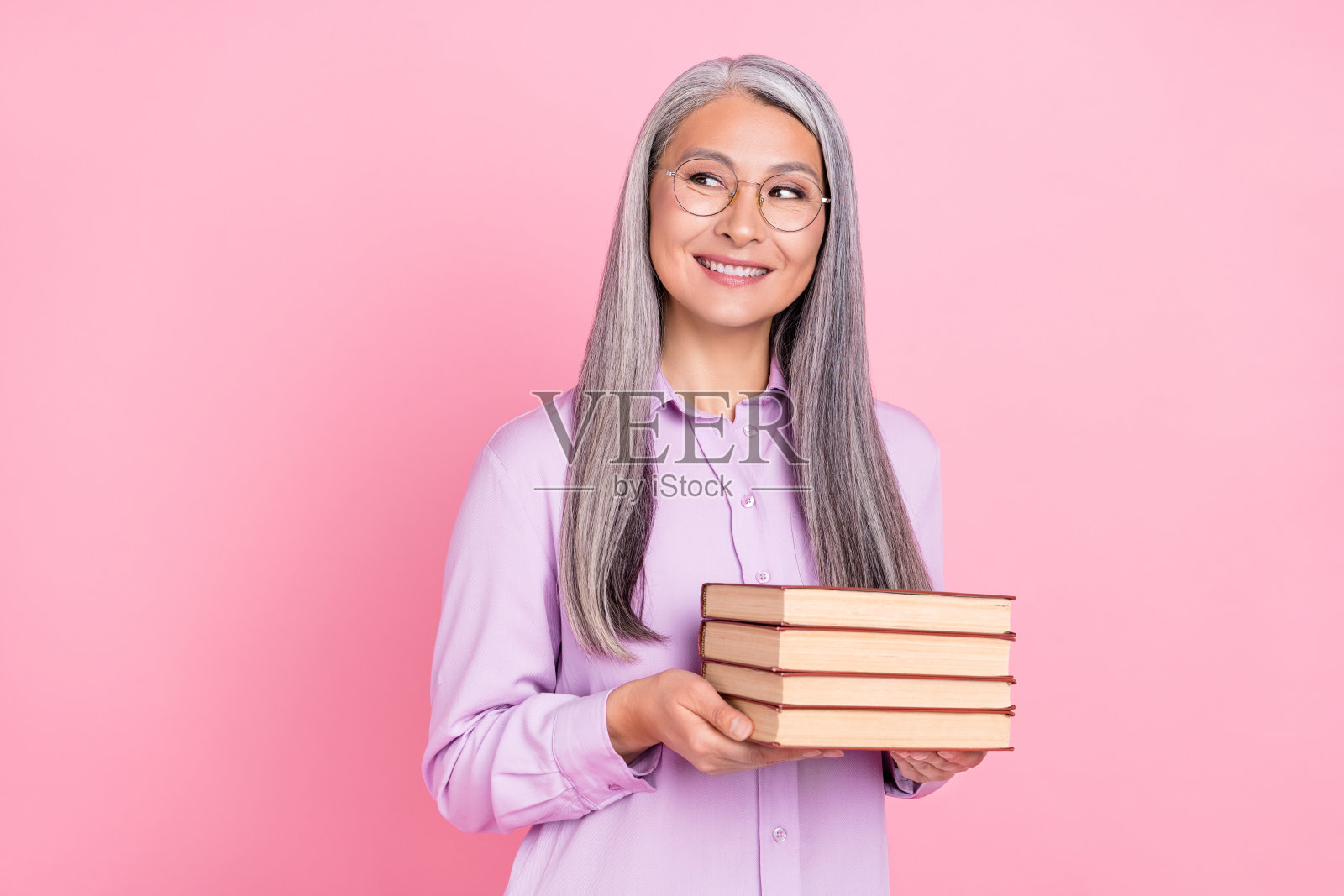 一位迷人、开朗的灰发女性手持书籍，思考着，背景为粉色柔和色调，留有空白空间。照片摄影图片