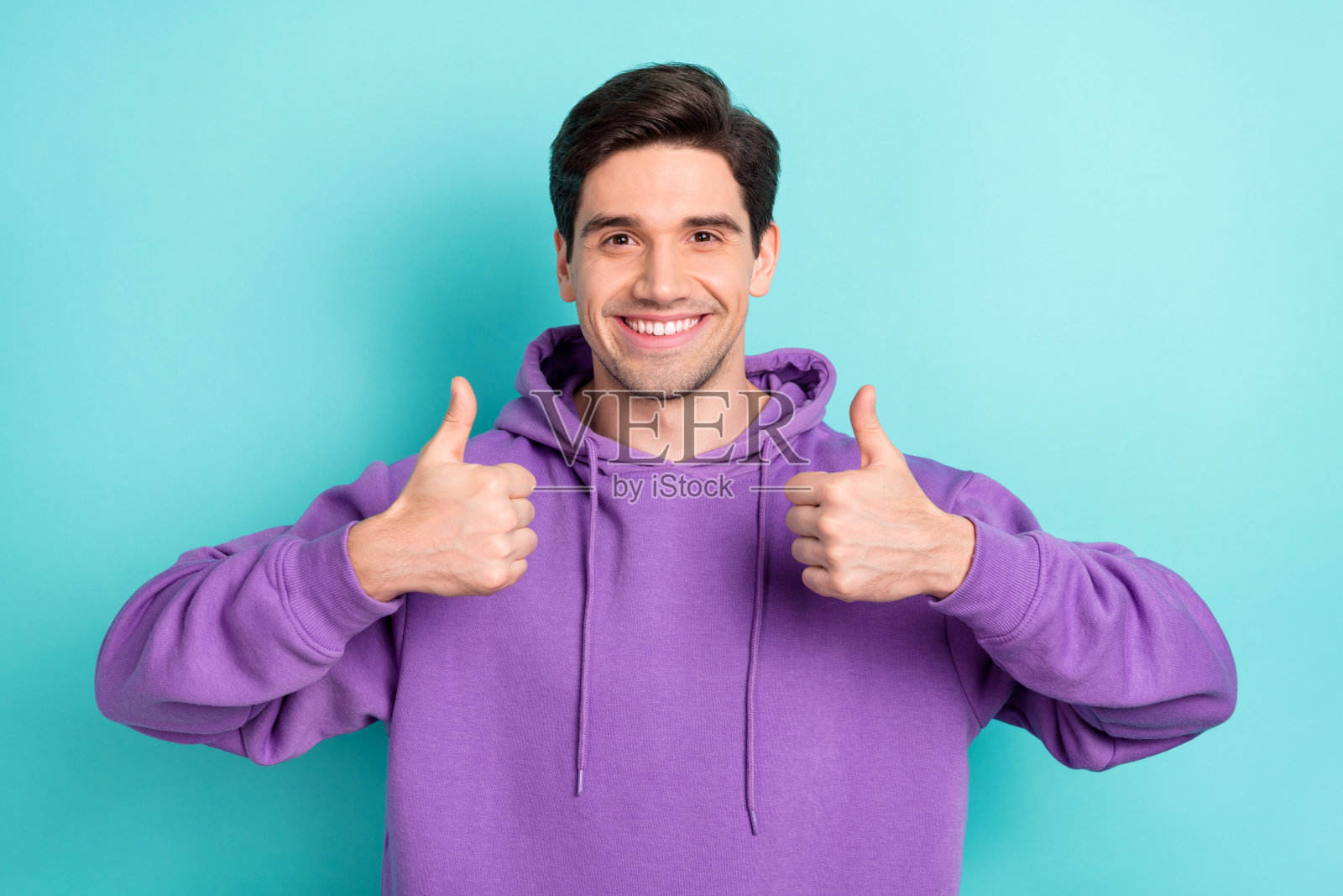 穿着紫色连帽衫的时尚街头风格男孩在蓝色背景下竖起大拇指推荐。照片摄影图片