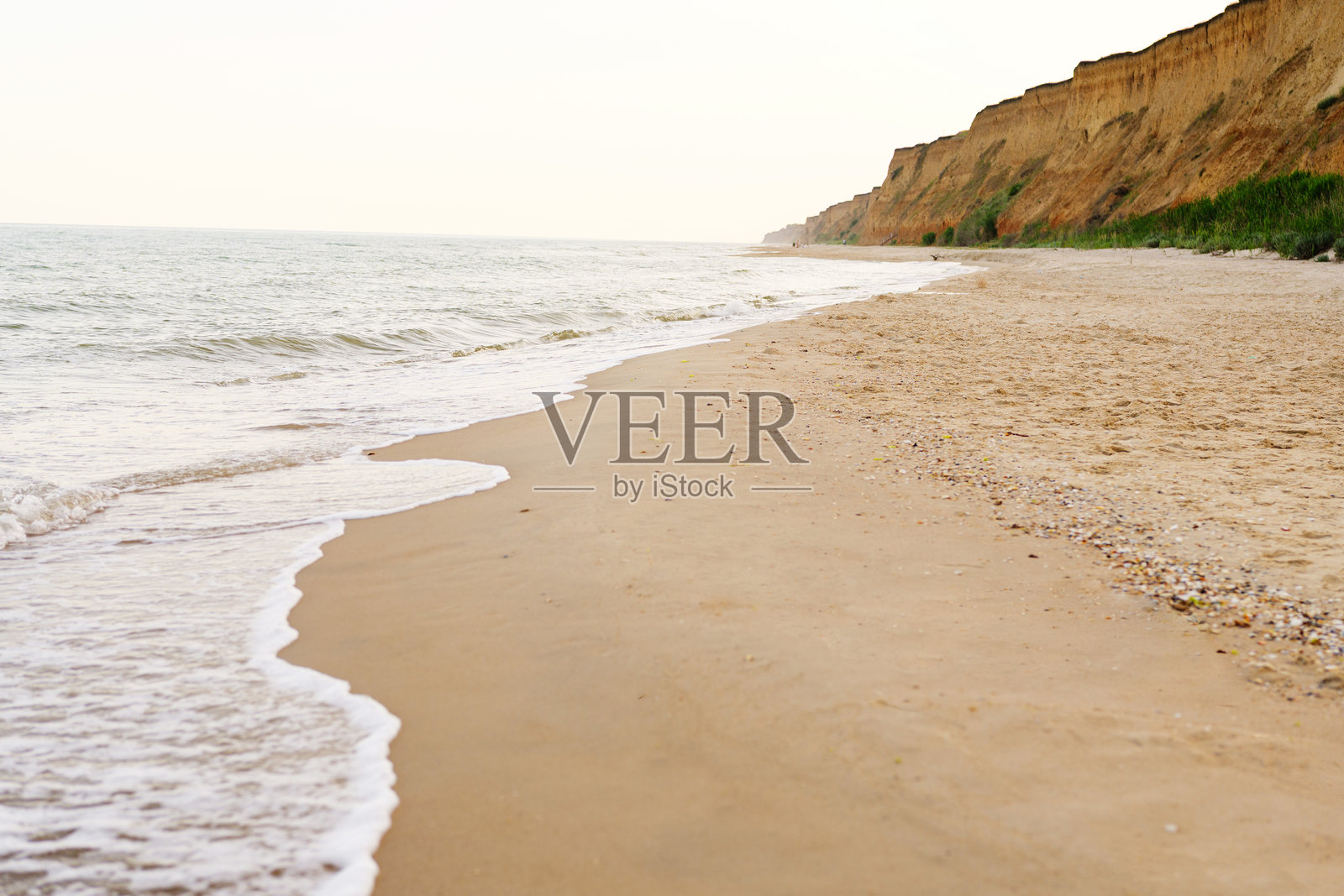 沙滩上轻柔的海浪与高耸的侵蚀海岸悬崖相伴。宁静的海边。照片摄影图片